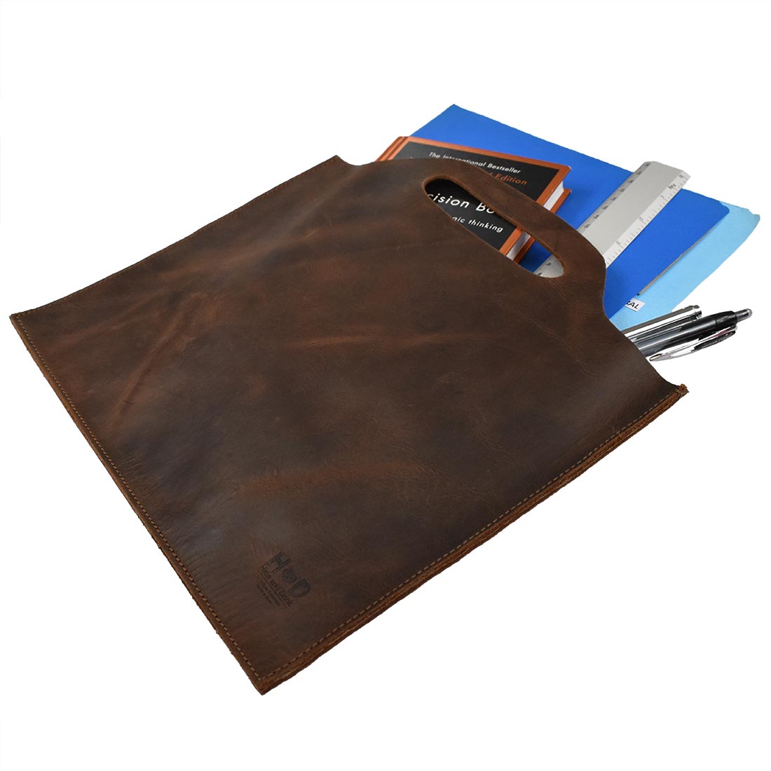 Flat Handbag by Hide & Drink, demonstrating its versatile use as a thin portfolio with documents and a ruler. This full grain leather bag serves as a minimalist style carry-on bag and classic document holder, showcasing the quality of small batch production. Hand cut, hand sewn, and fire branded, this artisan piece is handmade in La Antigua Guatemala & Oaxaca Mexico.