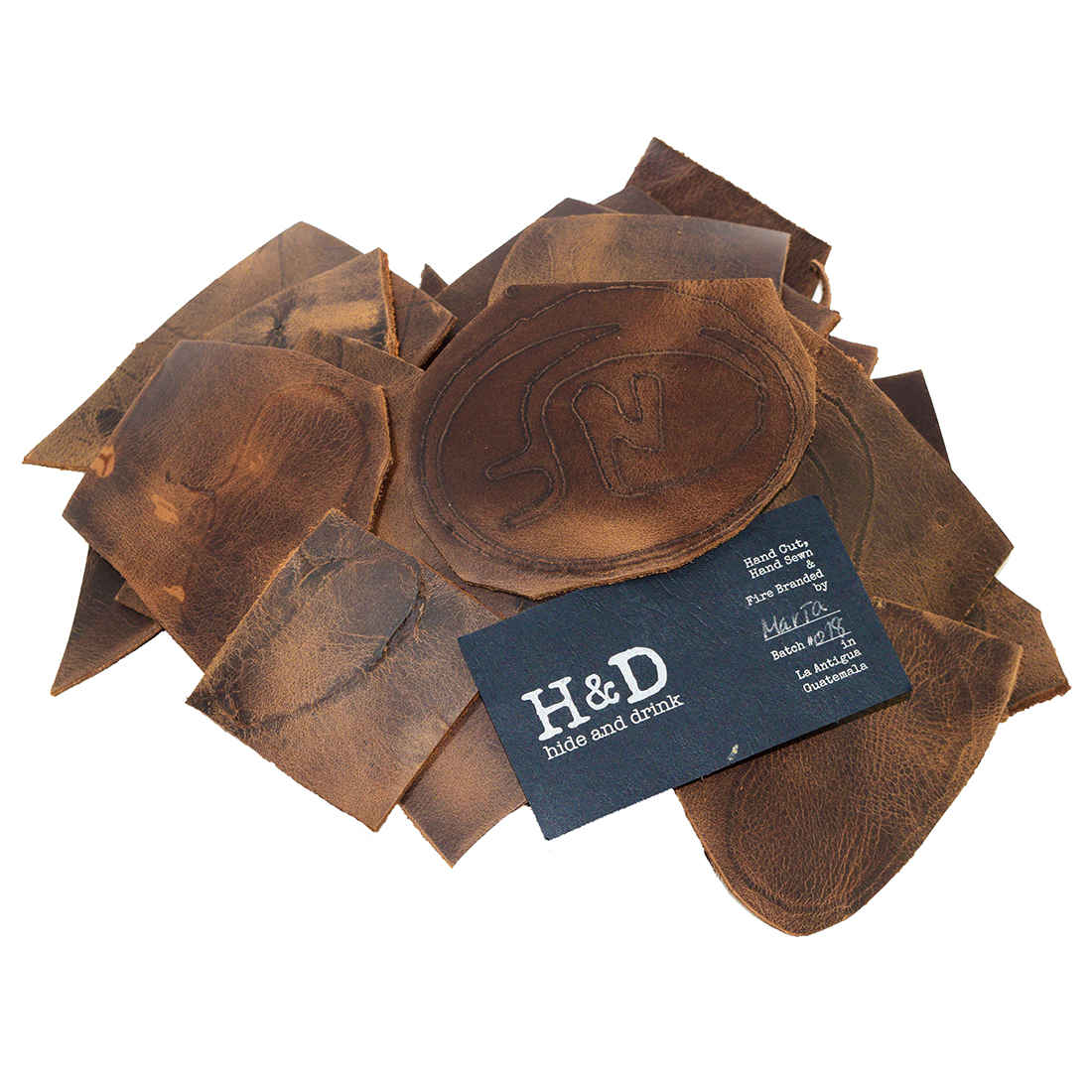 Hide & Drink Leather Scraps With Scars (12 oz pack) displaying an assortment of quality full grain leather pieces. Handcrafted by artisans, these leather scraps offer a perfect solution for arts & crafts. Included are 8 inches long scraps in various widths, showcasing unique scars. Every piece is small batch produced and hand sewn, made with care in La Antigua Guatemala, ensuring a truly authentic crafting experience.