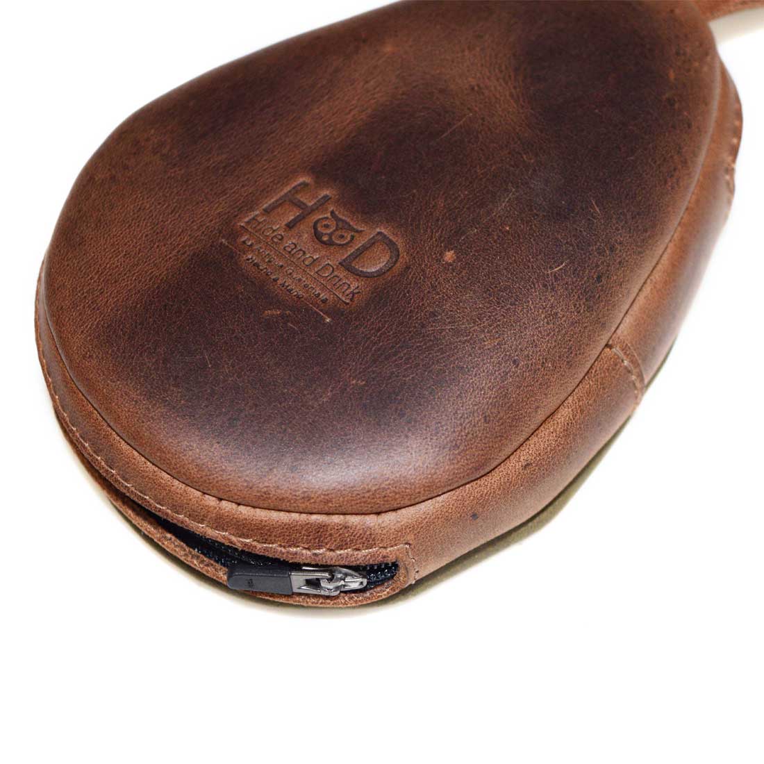 Hide & Drink Avocado Purse, displaying a close-up of the durable zipper and artisan branding. This avocado-themed case bag is perfect for organizing coins, cards, and money, making it a lovely cute gift. Each piece is made from full grain leather through small batch production methods, hand cut and hand sewn, fire branded by skilled artisans in La Antigua Guatemala & Oaxaca Mexico.
