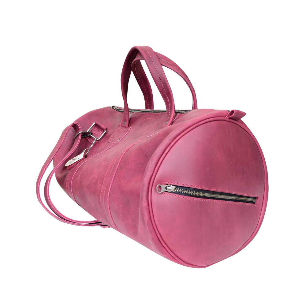 Side view of the Classic Duffle Bag by Hide & Drink in pink leather, demonstrating its classic design with an adjustable strap and zipper closure. This Full Grain Leather Classic Duffle Bag is a perfect Messenger Bag option for travel, handmade in La Antigua Guatemala & Oaxaca Mexico.