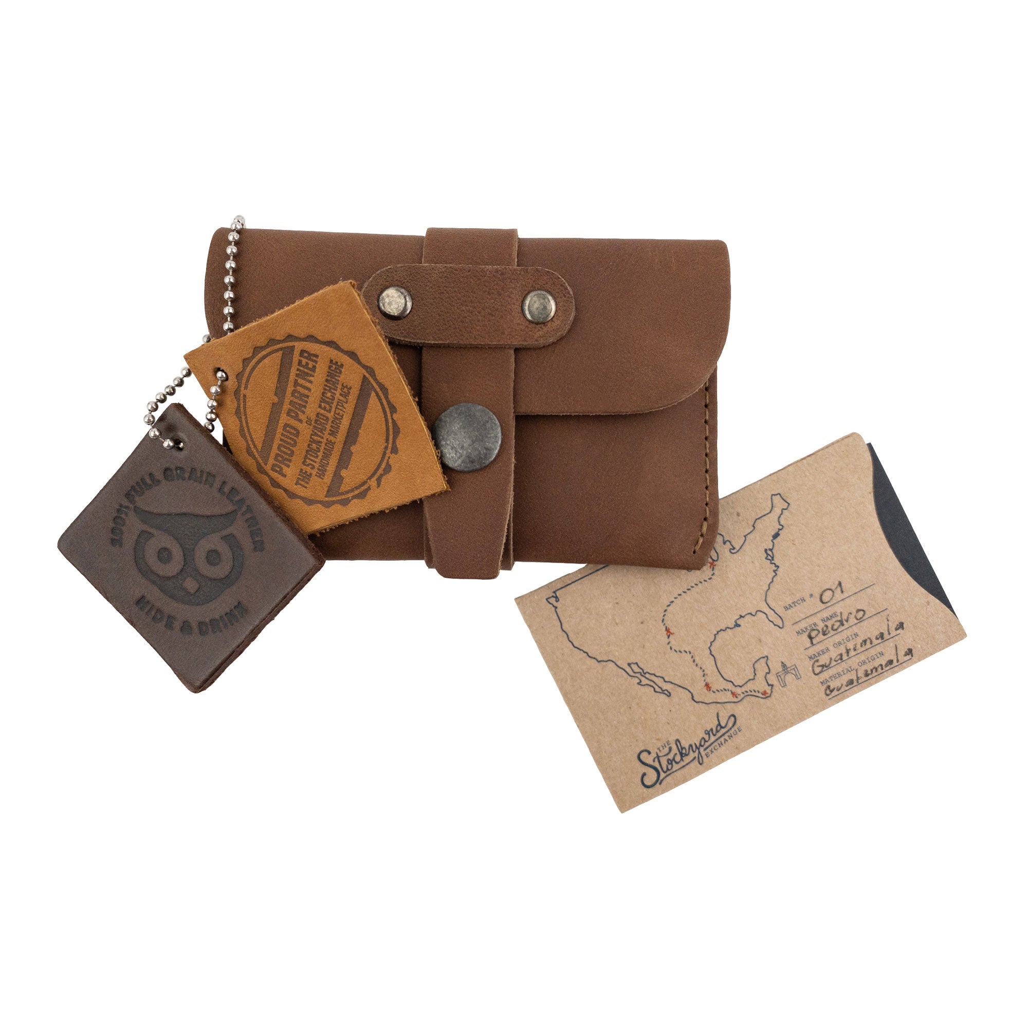 Hide & Drink's brown Credit Card Holder displayed with accompanying artisan tags. This Full Grain Leather wallet is a perfect blend of functionality and elegant design, showcasing craftsmanship from La Antigua Guatemala.