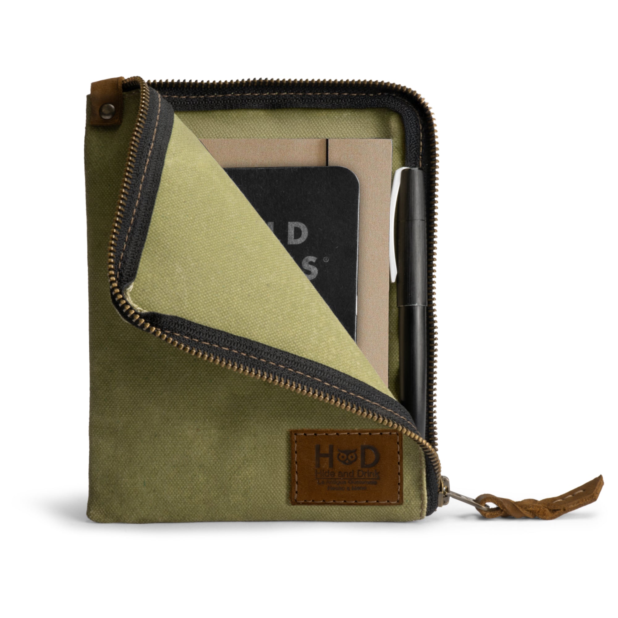 Front view of the green Scribbler Case from Hide & Drink, crafted from Waxed Canvas. Ideal for holding notebooks, emphasizing small batch production, hand cut, hand sewn, and artisan quality. Handmade in La Antigua Guatemala & Oaxaca Mexico.