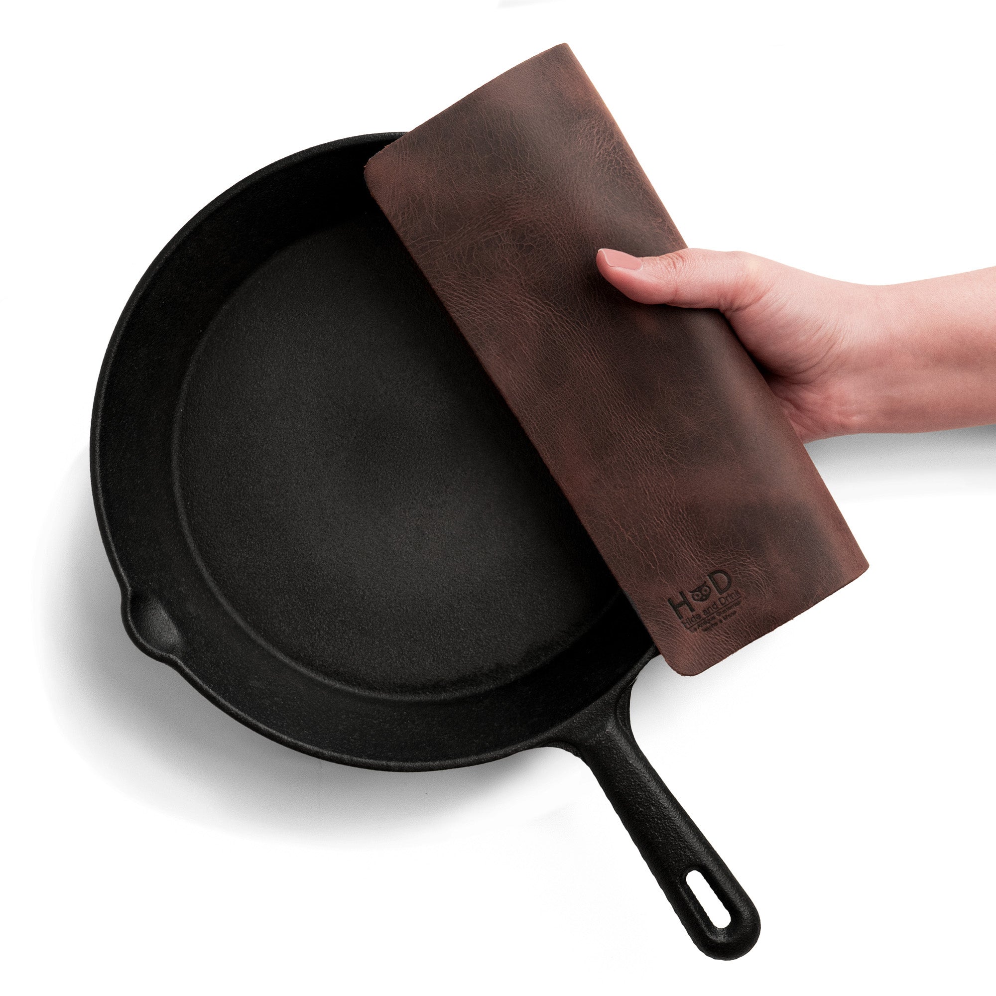Hide & Drink's Potholder Sheet held over a cast iron skillet, showcasing its sturdy design and full grain leather materials. This Squared Potholder Sheet is essential for cookware, blending durability with style, making it ideal for kitchen and bakery supplies. Handmade in La Antigua Guatemala & Oaxaca Mexico, it features artisan craftsmanship with a fire-branded logo.