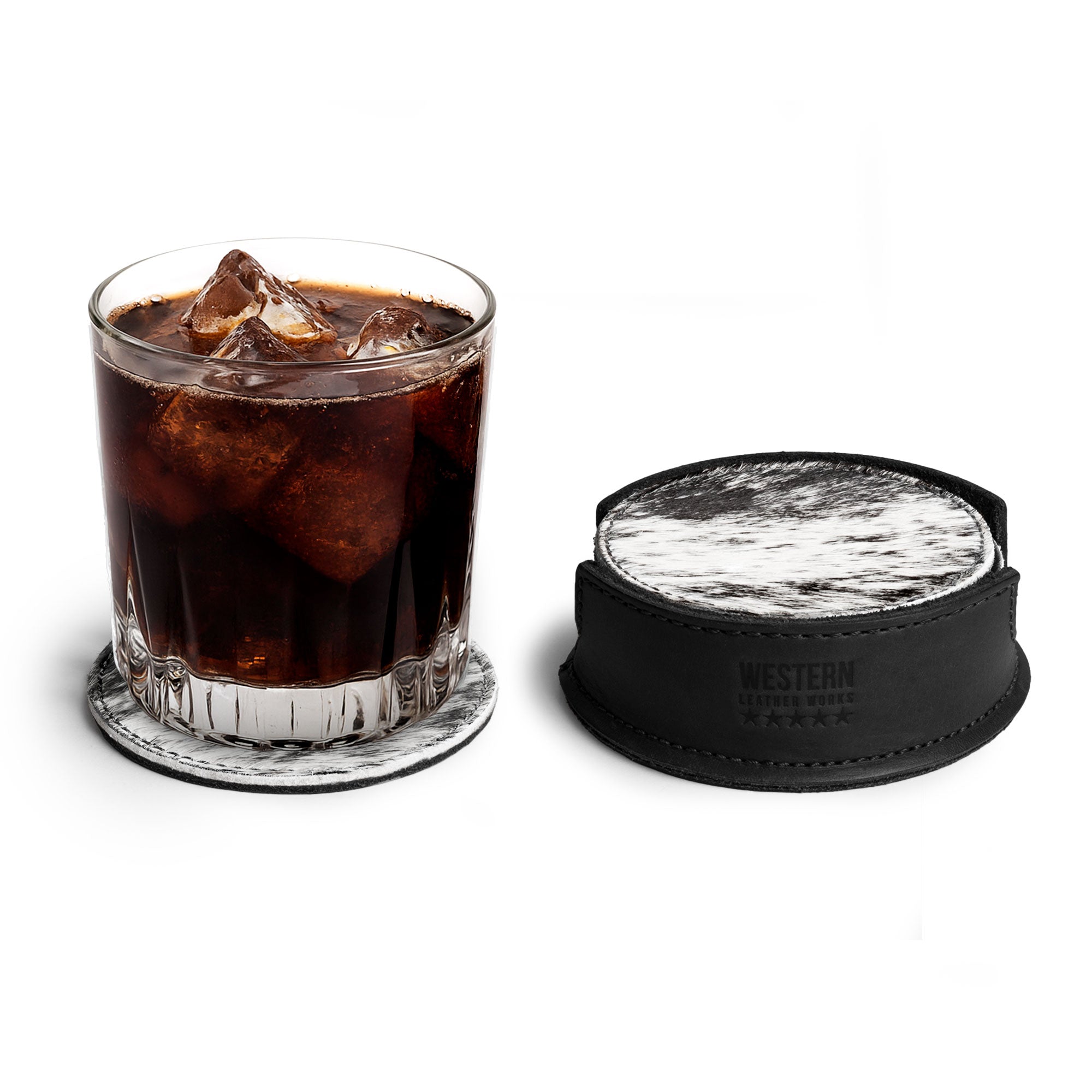 A glass of dark beverage positioned on a hair-on-hide coaster from Western Leather Works, as part of the Set of 6 Circular Coasters for Drinks, designed for effective Glass & Cups Stain Protection. This artisan product features Full Grain Leather, crafted through small batch production that showcases hand cut and hand sewn techniques, along with fire branding, emphasizing its handmade origins in La Antigua Guatemala & Oaxaca Mexico.