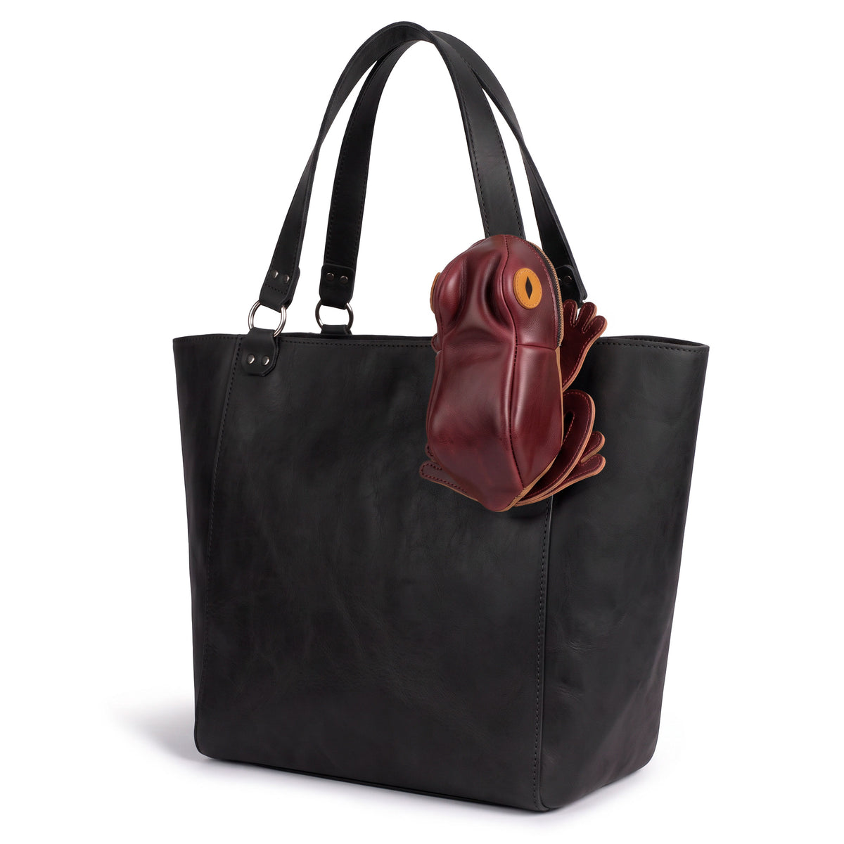 Tudi Frudi Frog Pouch shown attached to a black tote bag, featuring a Frog-Shaped Pouch design made as a Cable Organizer and Small Accessory Case, plus a Zippered Cash Holder Wallet for Coins and Change Purse. This Full Grain Leather accessory is designed as Pouches for Men and Women, made through StockyardX Small Batch Production with Hand Cut, Hand Sewn, Fire Branded, Artisan craftsmanship, Handmade in La Antigua Guatemala & Oaxaca Mexico.