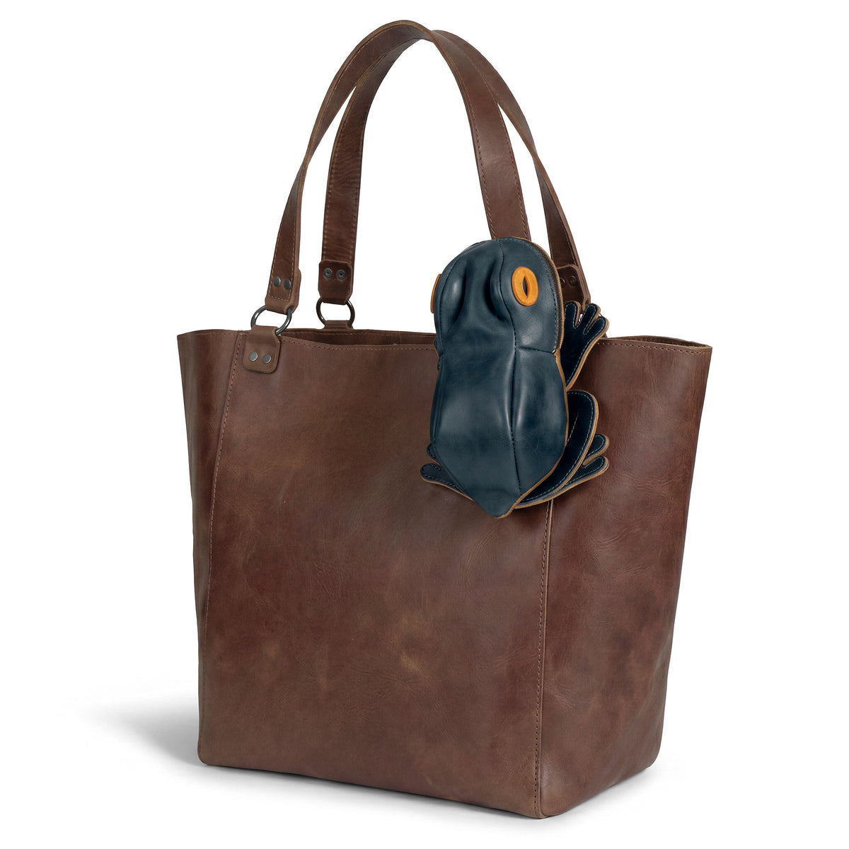 Tudi Frudi Frog Pouch displayed on a leather tote, a Frog-Shaped Pouch that works as a Cable Organizer, Small Accessory Case, Zippered Cash Holder Wallet for Coins, or Change Purse. This versatile option for Pouches for Men and Women is made from Full Grain Leather through StockyardX Small Batch Production, Hand Cut and Hand Sewn by Artisan makers, Handmade in La Antigua Guatemala & Oaxaca Mexico, with a Fire Branded finish.
