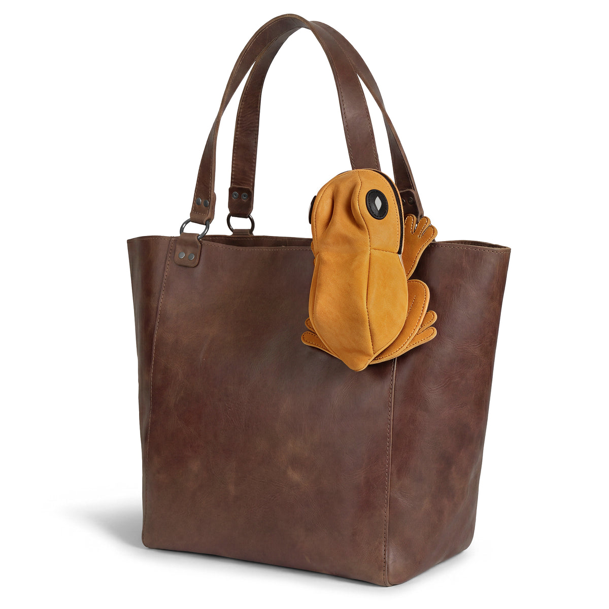 Tudi Frudi Frog Pouch hanging from a leather tote, featuring a Frog-Shaped Pouch design made as a Cable Organizer and Small Accessory Case; a Zippered Cash Holder Wallet for Coins and Change Purse, ideal as Pouches for Men and Women. Crafted from Full Grain Leather through StockyardX Small Batch Production, this Hand Cut, Hand Sewn, Fire Branded Artisan piece is Handmade in La Antigua Guatemala & Oaxaca Mexico.
