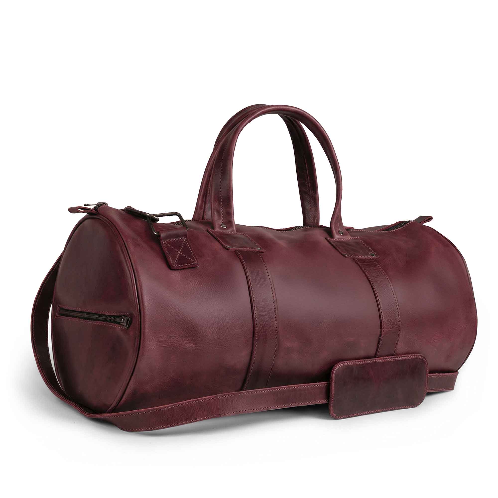 Side view of the Classic Duffle Bag by Hide & Drink in pink leather, demonstrating its classic design with an adjustable strap and zipper closure. This Full Grain Leather Classic Duffle Bag is a perfect Messenger Bag option for travel, handmade in La Antigua Guatemala & Oaxaca Mexico.