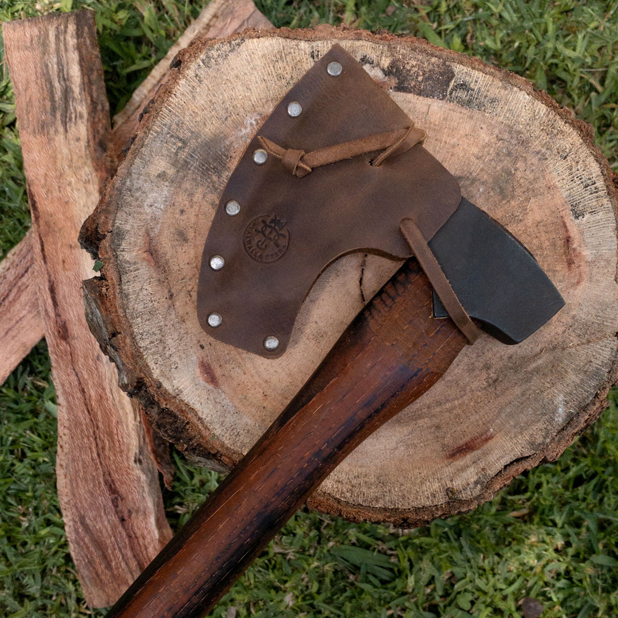 Display of the Axe Head Sheath with String by Valhalla Gear on a wooden tree stump, highlighting its handcrafted details. Made from full grain leather, this handmade accessory adds elegance to your axe collection, and is ideal for bikers looking for a stylish universal saddlebag.