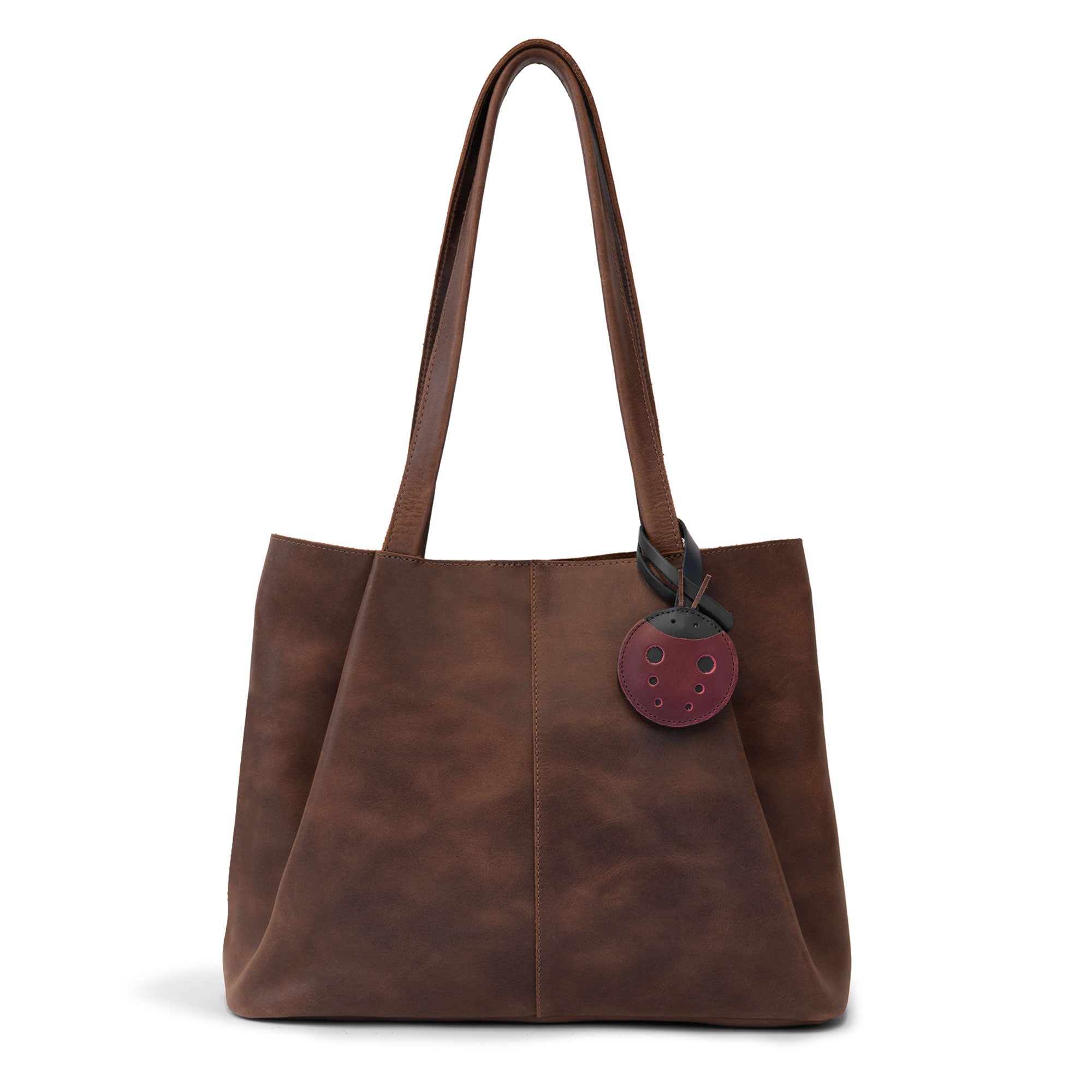 Hide & Drink Bag Charms attached to a stylish brown handbag, displaying a pineapple design perfect for personalization. This accessory serves as a purse charm for tote & backpacks made from durable full grain leather, demonstrating StockyardX's commitment to small batch production. Each piece features hand cut, hand sewn artistry and fire branding, handmade in La Antigua Guatemala & Oaxaca Mexico.