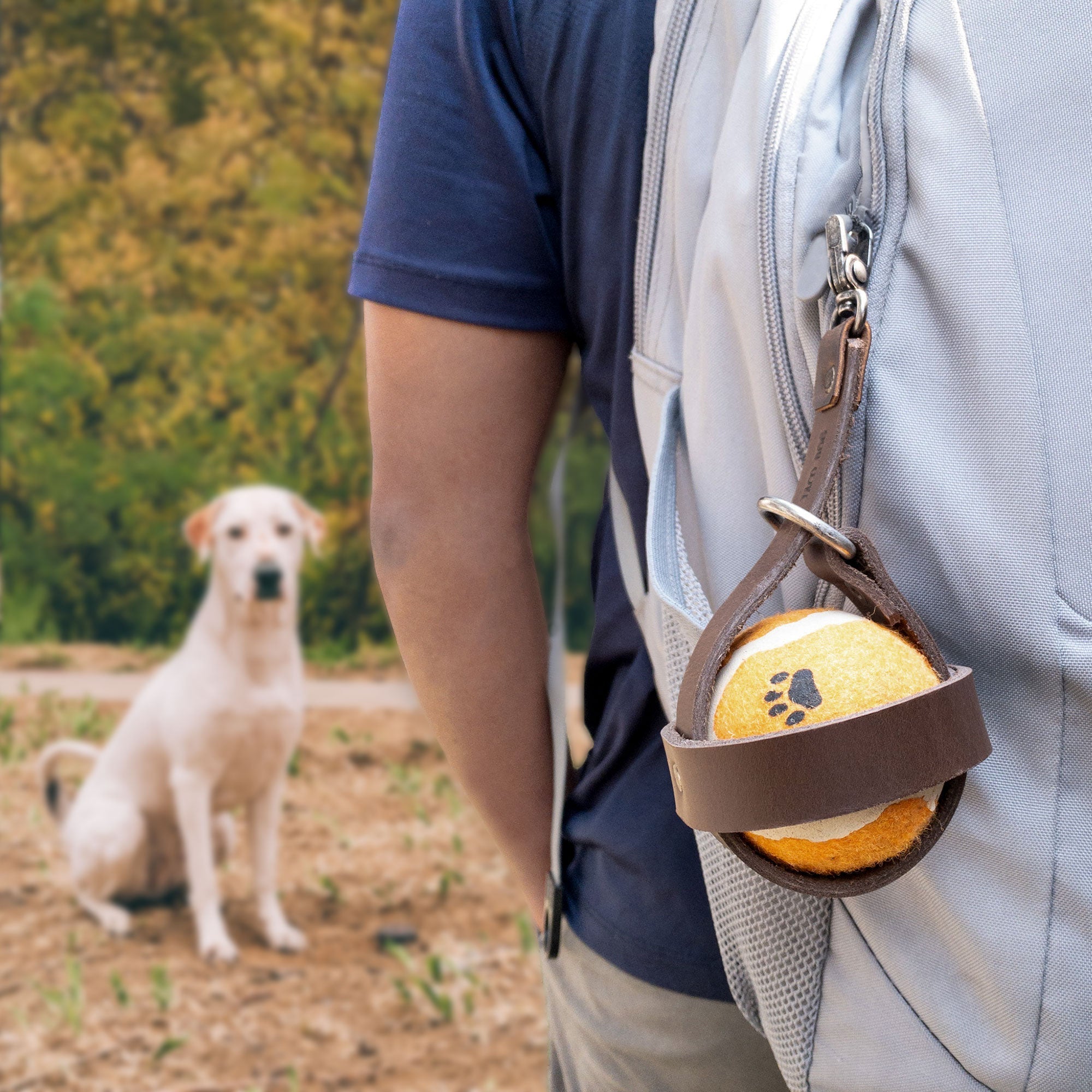 A person wearing a backpack with the Taco Dog Dog Ball Holder conveniently attached, showcasing its functionality as a Leash Attachment Case for easy access to the pet toy. Ideal for outdoor settings, this durable Chasing Pet Toy Storage is made from Full Grain Leather, emphasizing the Artisan quality and Handmade craftsmanship in La Antigua Guatemala.