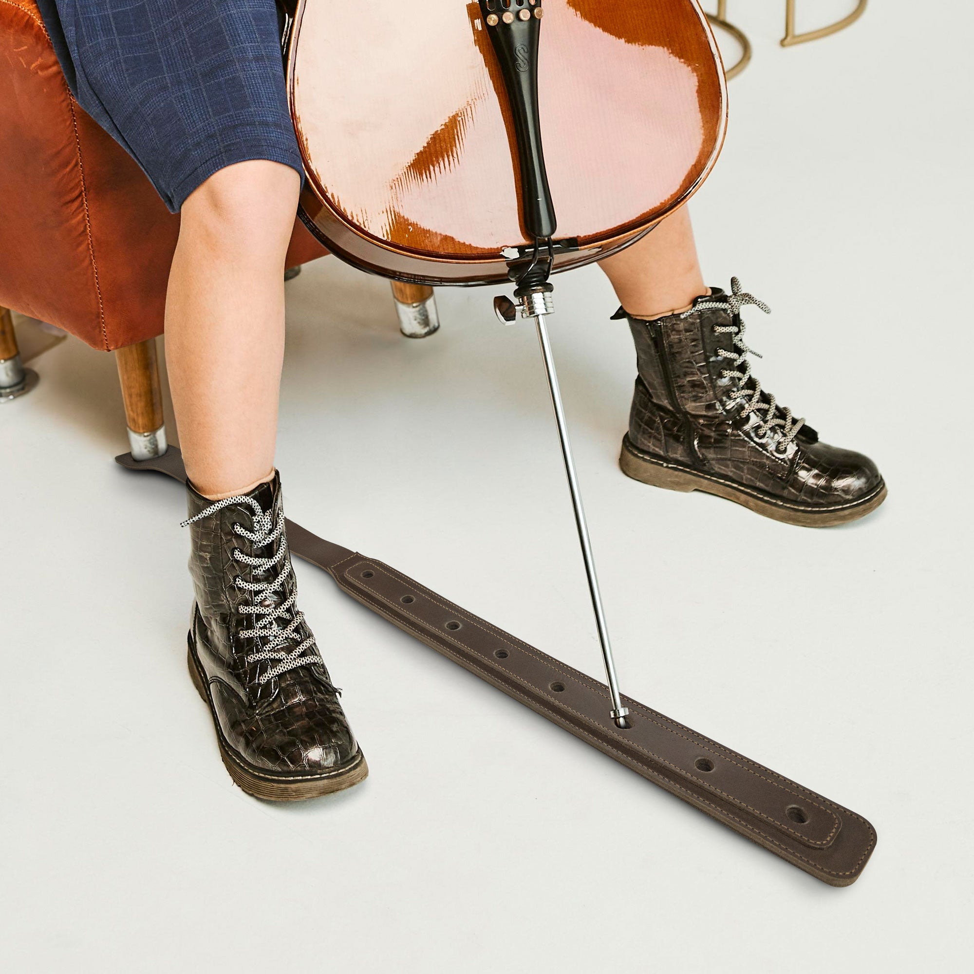 A Cello Endpin Strap Stopper in action, shown with a cello and a musician’s stylish boots. This Classic Non-Slip Stopper by tocame ensures stability and protects floors while practicing. Made from durable full grain leather, this artisan accessory exemplifies small batch production and handcrafted excellence.