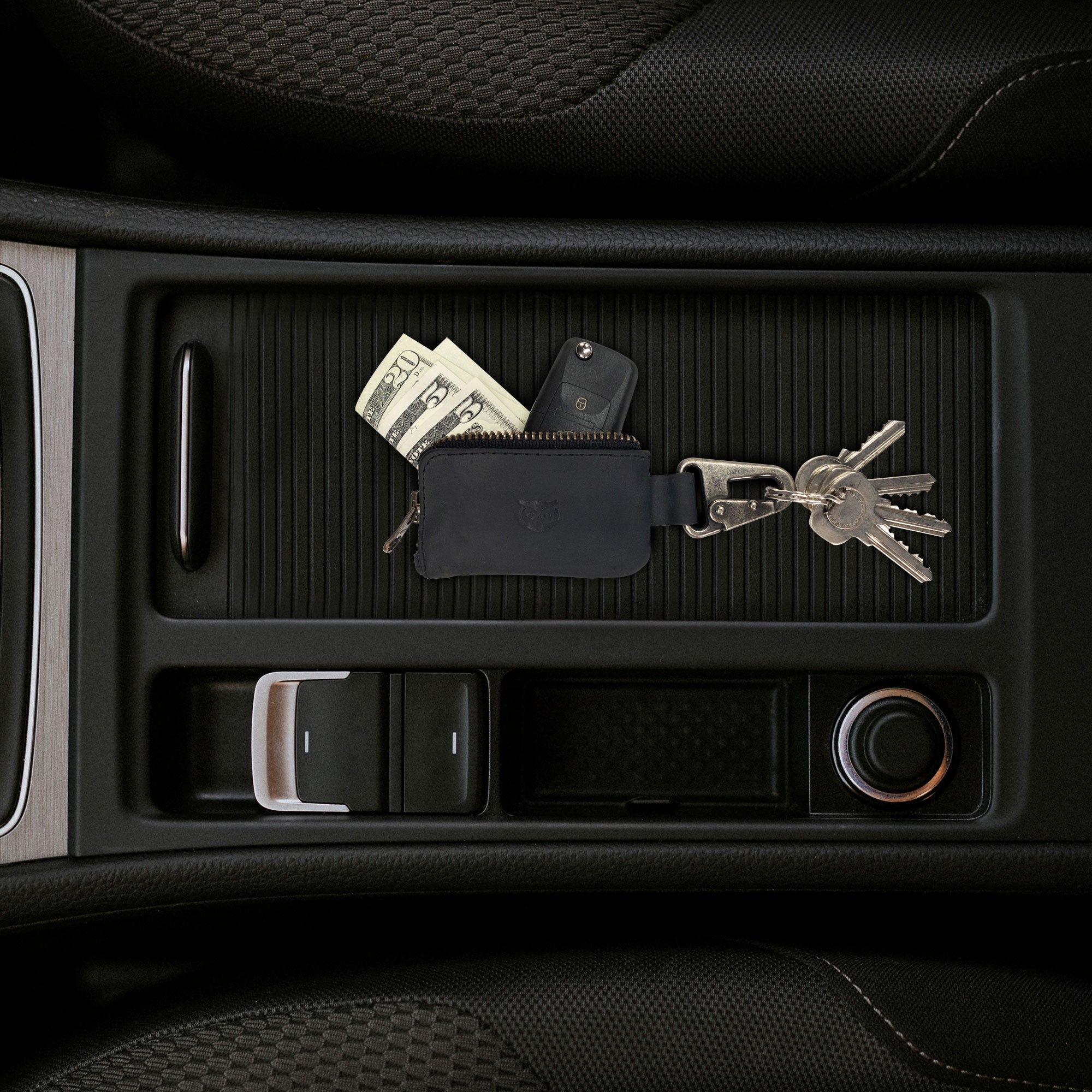 The Car Key Holder by Hide & Drink is shown conveniently placed in a car console, demonstrating its practical design. This Car Key Holder not only holds your car keys but also doubles as a cash zipper case for headphone and charging cables, memory cards, and flash drives, all secured by a nickel metal clasp. Enjoy high-quality craftsmanship through small batch production, hand cut, hand sewn artistry, handmade in La Antigua Guatemala & Oaxaca Mexico.