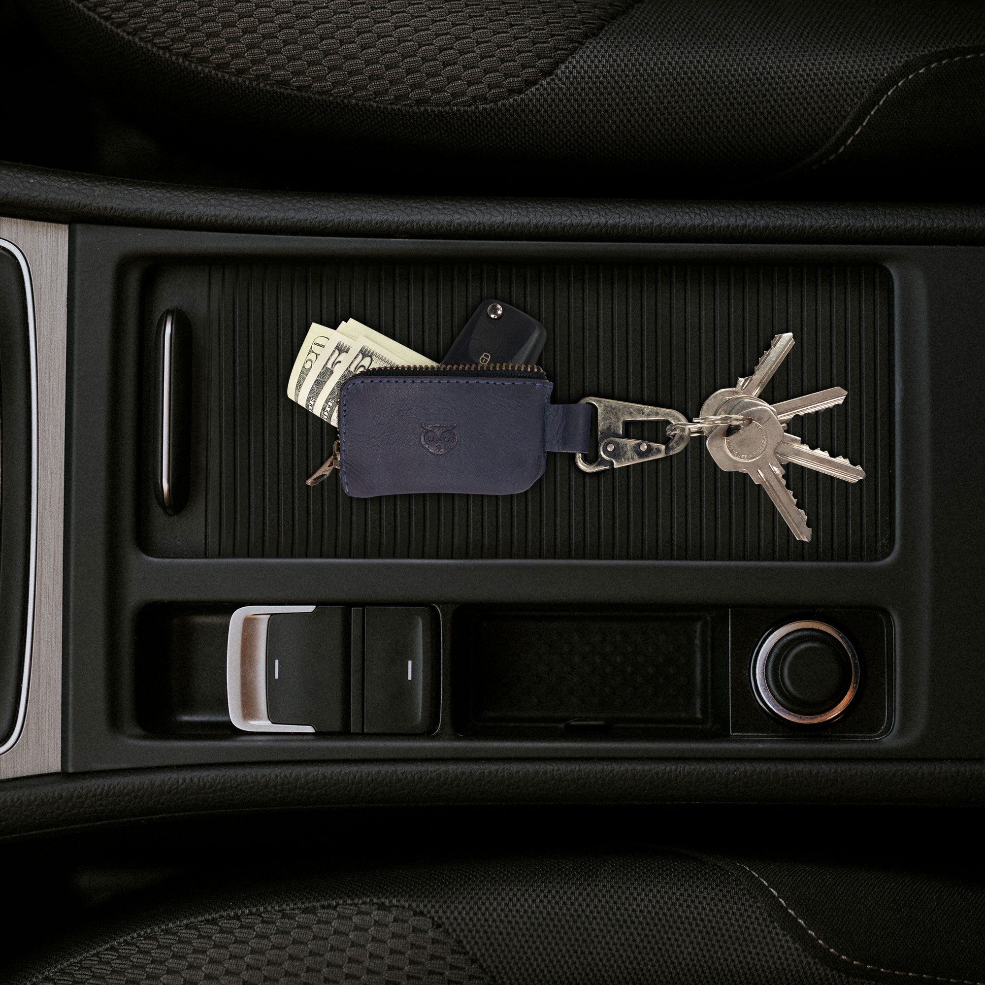 Hide & Drink Car Key Holder resting in a car console, showcasing its use as a Cash Zipper Case with a Nickel Metal Clasp, ideal for holding headphone and charging cables, memory cards, and flash drives, crafted from full grain leather with an artisan touch. StockyardX, Small Batch Production, Hand Cut, Hand Sewn, Fire Branded, Handmade in La Antigua Guatemala & Oaxaca Mexico.