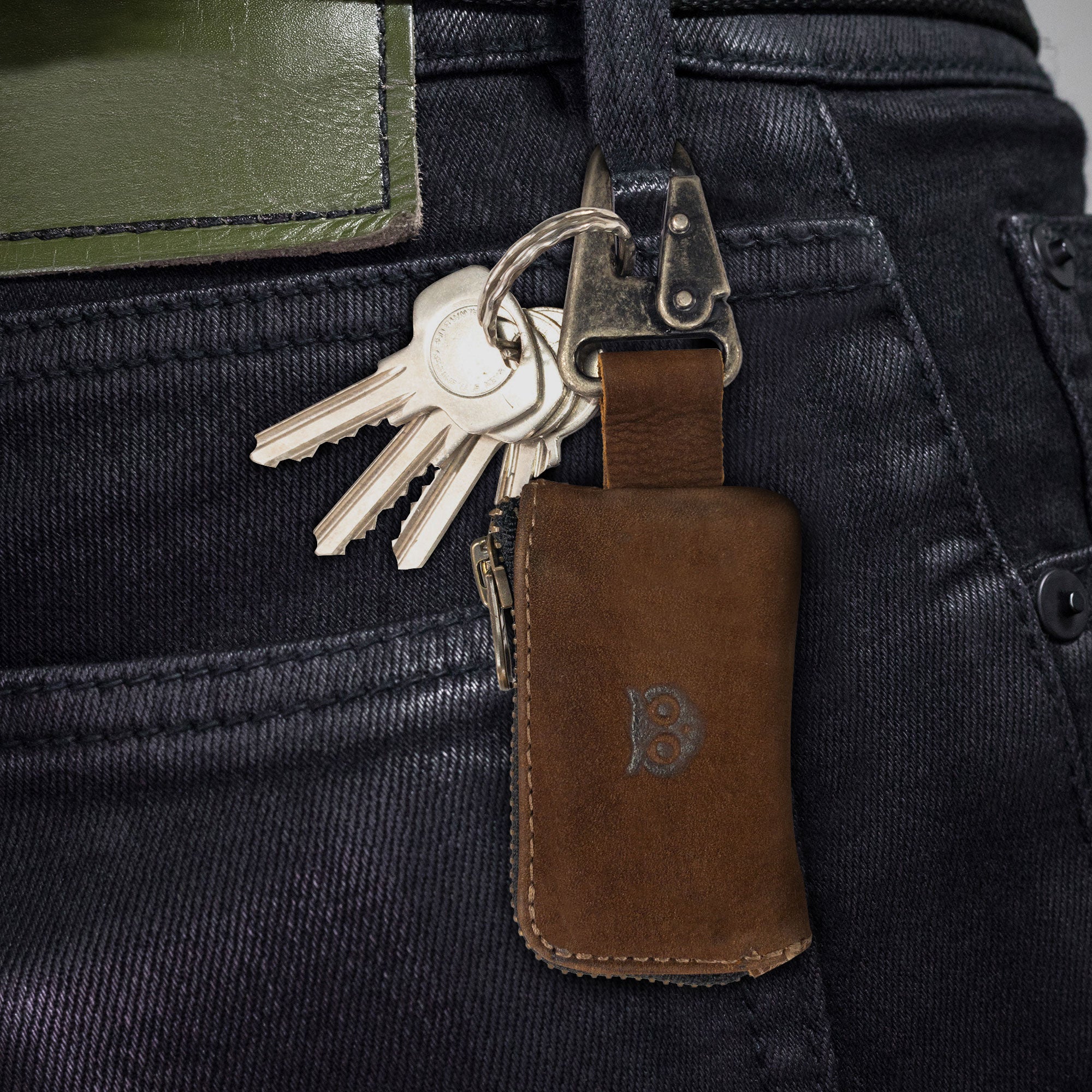 A stylish Car Key Holder by Hide & Drink, showcasing a rustic leather key fob attached to a belt loop, perfect for secure storage. This Car Key Holder allows you to carry headphone and charging cables, memory cards, flash drives, or cash in its zipper case secured with a nickel metal clasp, made from full grain leather. Ideal for those who appreciate small batch production, hand cut, hand sewn craftsmanship, and artisan quality, handmade in La Antigua Guatemala & Oaxaca Mexico.