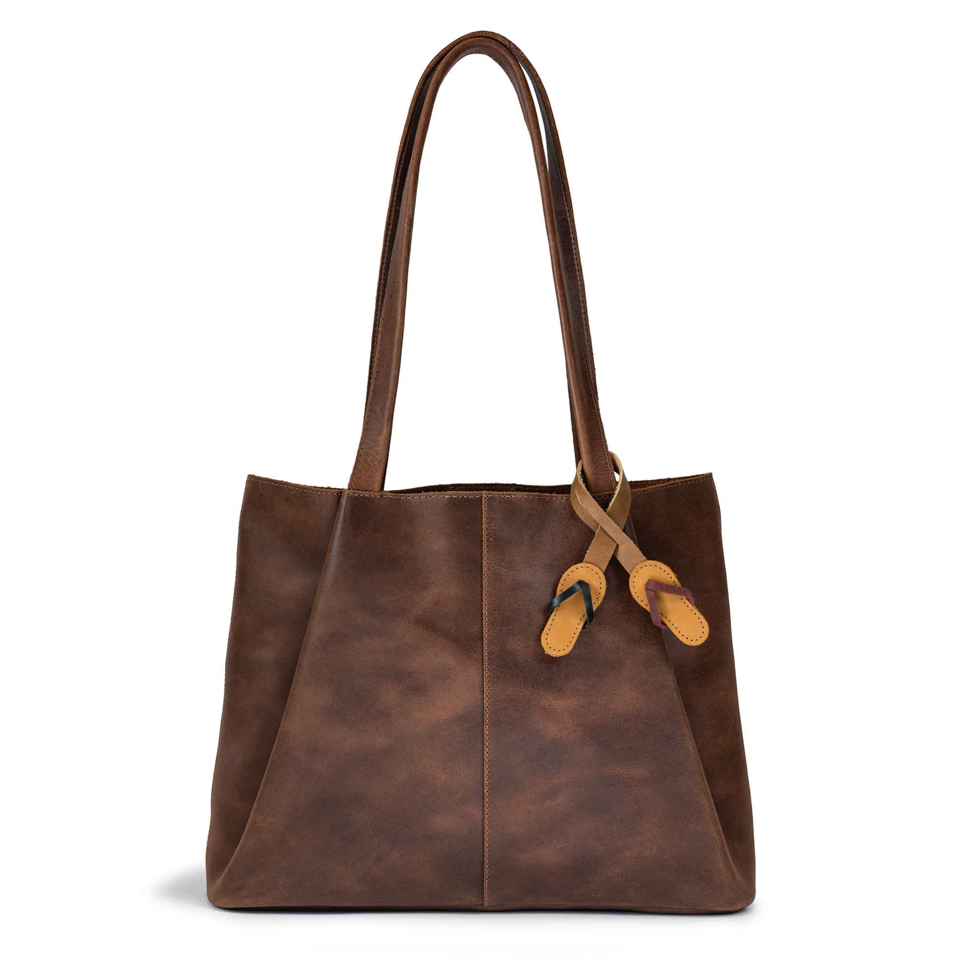 Hide & Drink Bag Charms attached to a brown handbag, featuring a flip flop design perfect for personalization. This purse charm for tote & backpacks is made from full grain leather, demonstrating StockyardX's commitment to small batch production. Each piece showcases hand cut, hand sewn quality and fire branded artisan craftsmanship, handmade in La Antigua Guatemala & Oaxaca Mexico.