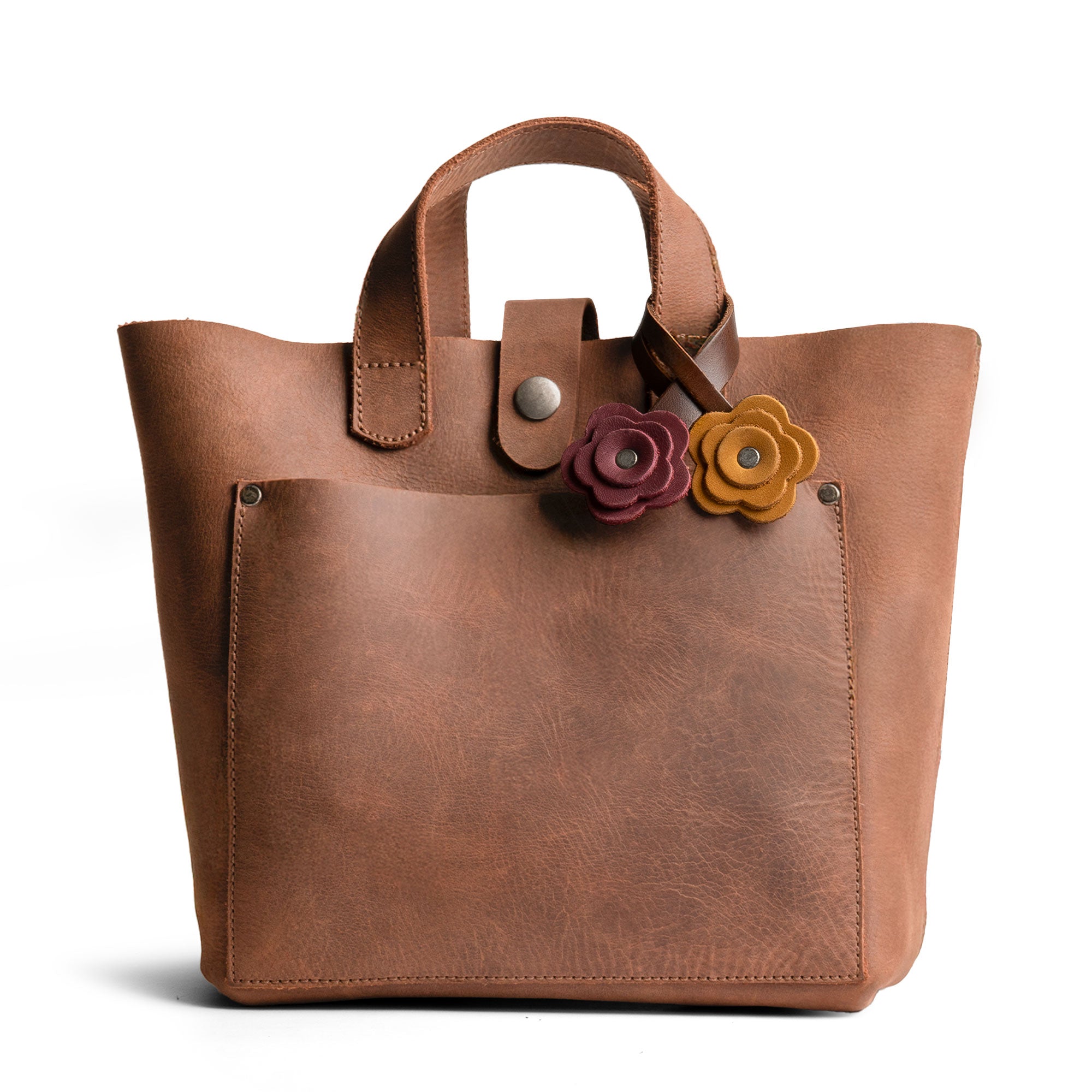 Showcasing the Rose Bag Ornament by Hide & Drink on a leather tote bag, this Full Grain Leather Rose-Shaped Ornament enhances your bag with a cute charm, making it an ideal accessory for shopping and outings.