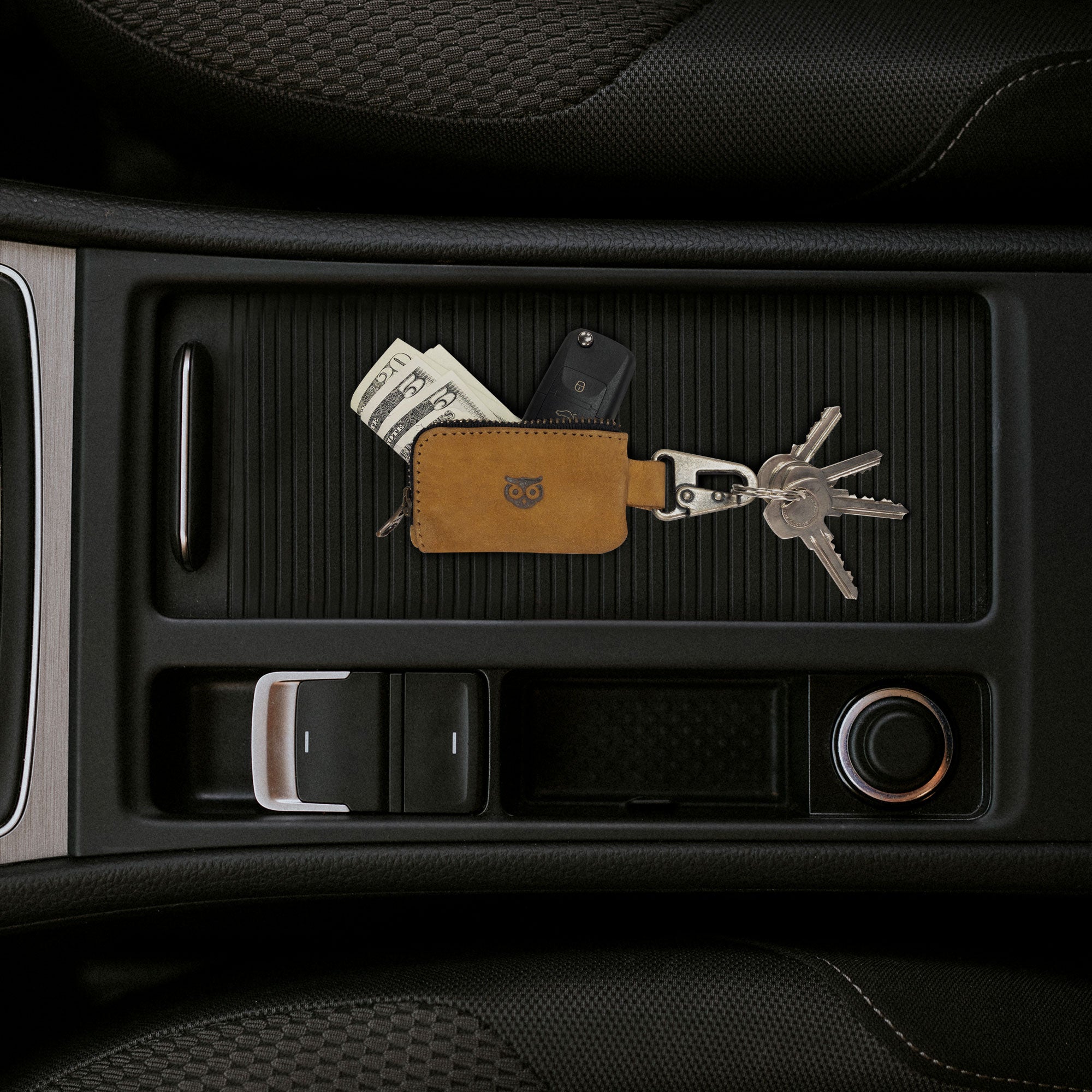 The Car Key Holder by Hide & Drink, shown with cash and keys in a vehicle's center console. This full grain leather accessory is perfect for holding items like headphone cables and flash drives, artisan made in La Antigua Guatemala & Oaxaca Mexico.