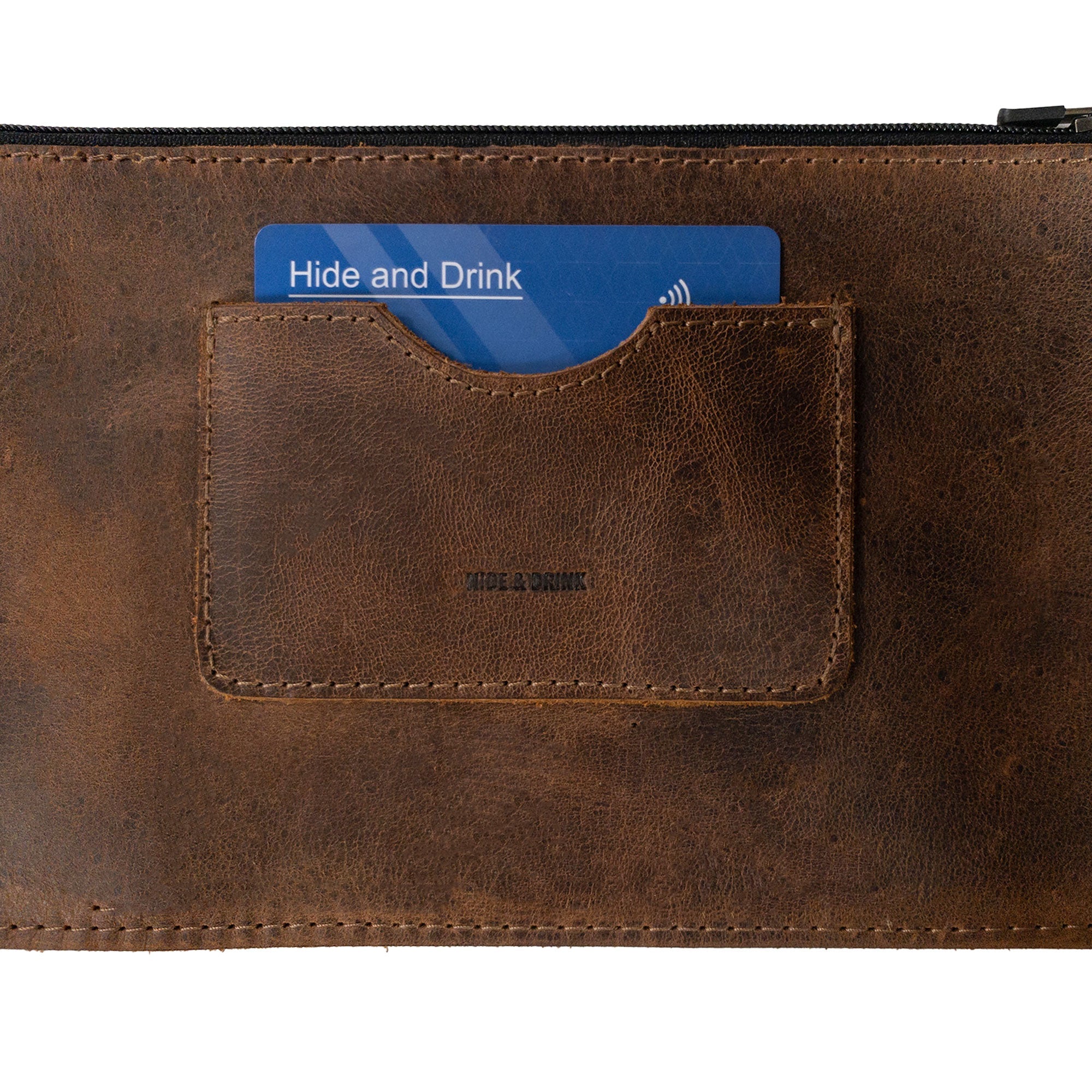Close-up of a brown rectangular zippered handbag by Hide & Drink, showing the card slot. This female purse is handcrafted from full grain leather, emphasizing the quality and small batch production techniques. The item features hand cut and hand sewn details, a fire branded logo, made with passion in La Antigua Guatemala & Oaxaca Mexico.