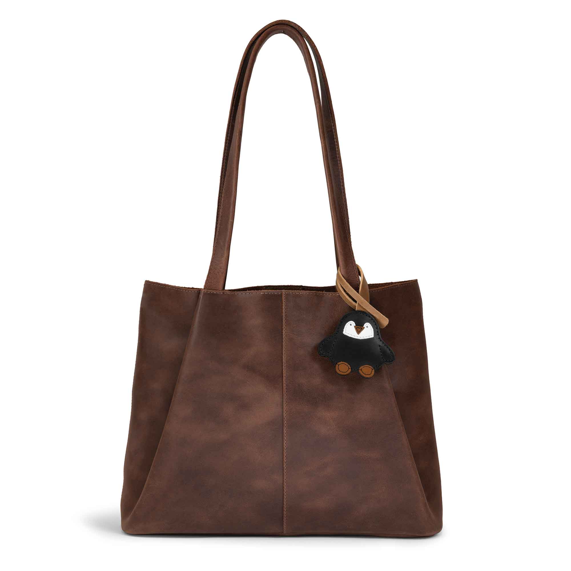 Hide & Drink Bag Charms attached to a stylish brown handbag, showcasing a heart design perfect for personalization. This purse charm for tote & backpacks made from full grain leather reflects StockyardX's commitment to small batch production. Each piece features meticulous hand cut, hand sewn craftsmanship and fire branding, handmade in La Antigua Guatemala & Oaxaca Mexico.