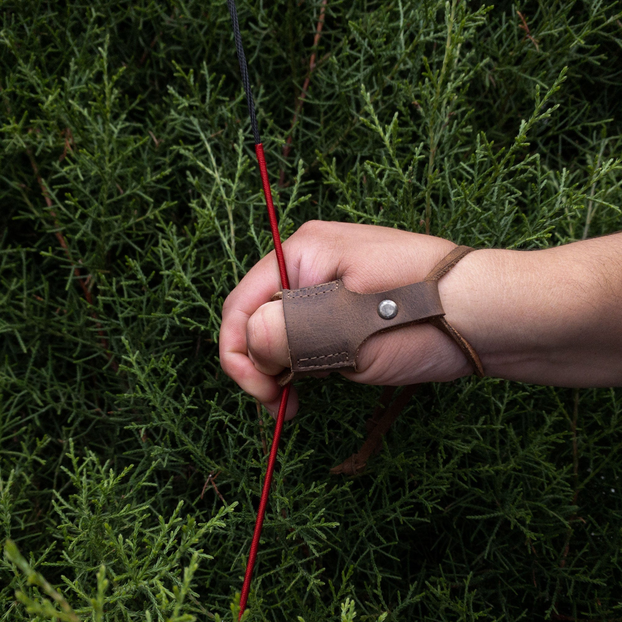A close-up of the Archery Thumb Finger Protector by Valhalla Gear in action, with a hand gripping an arrow. This handmade, artisan product is made of full grain leather, ensuring quality for shooting and training. An essential tool for both men and women receiving training in archery.
