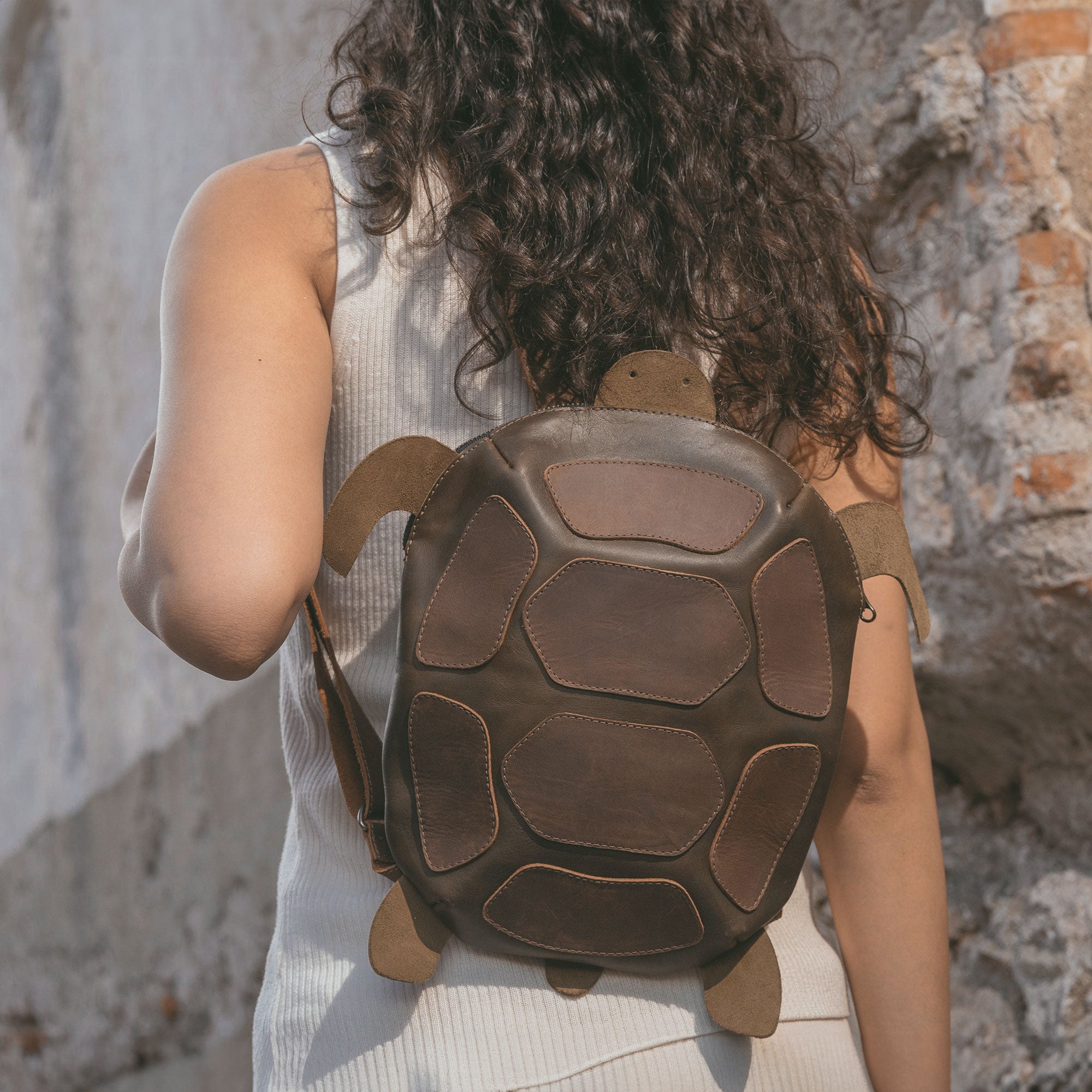 A person wearing the Turtle-Shaped Backpack by Hide & Play. This trendy bag is not only a Casual Bag but also functions as a Messenger Bag and Travel Bag for Men and Women. Crafted from Full Grain Leather, it represents StockyardX's Small Batch Production, showcasing artisan craftsmanship with precision hand cutting and hand sewing in La Antigua Guatemala.