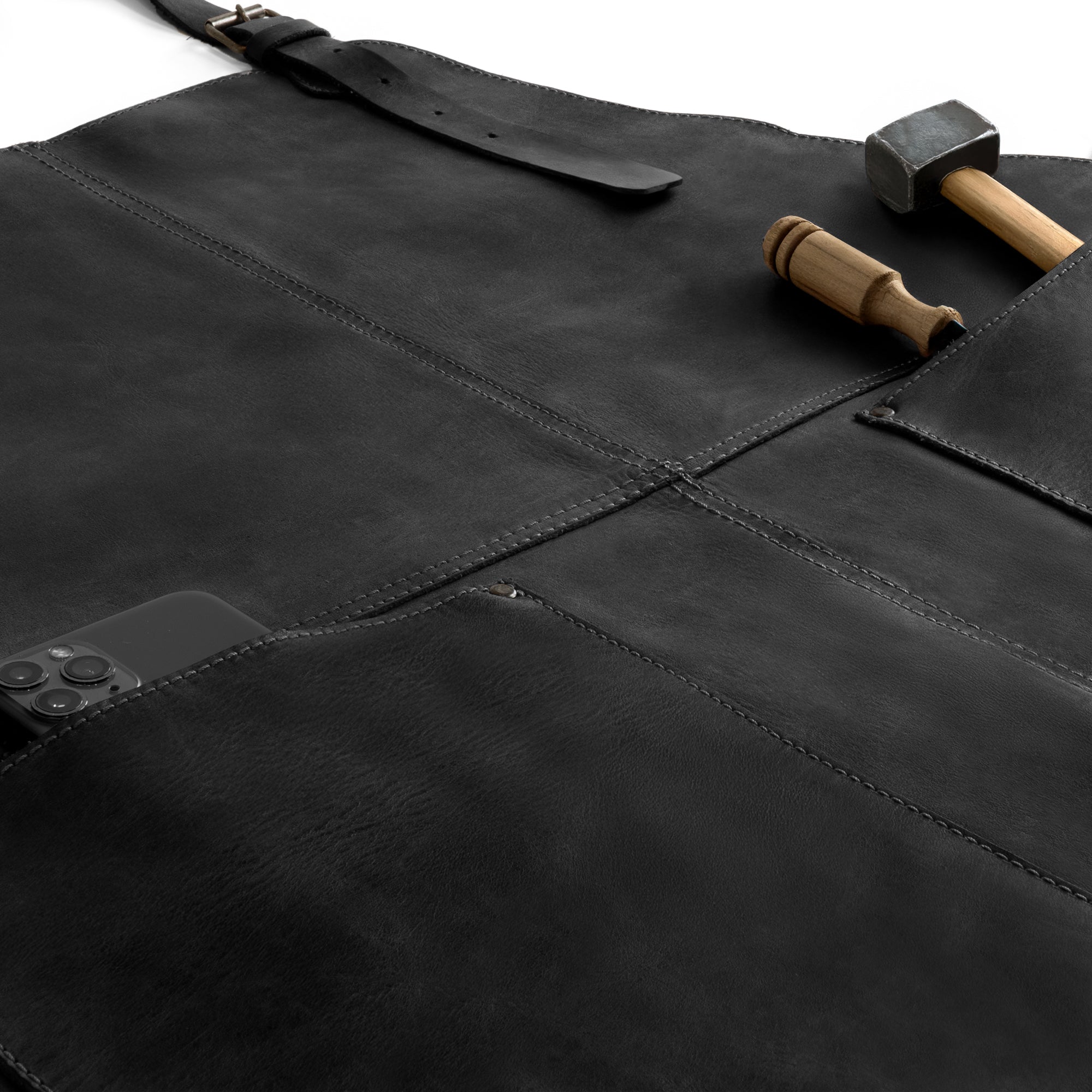 Close-up of the Hide & Drink Leather Apron in black, focusing on tools placed in its large pockets, emphasizing functionality. This durable Leather Apron is artisan-made from full grain leather for long-lasting use.