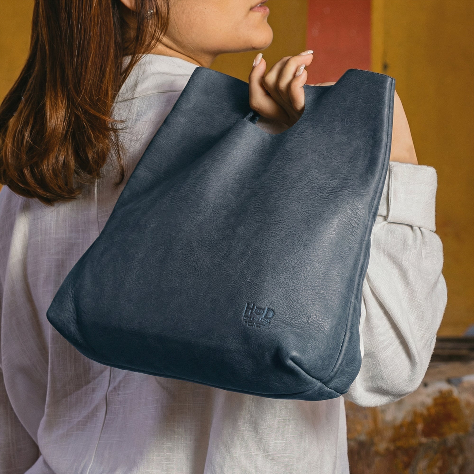 Hide & Drink Minimalist Boho Handbag on wooden surface with various everyday items, illustrating its spaciousness. This tote bag is an ideal shopping companion, handcrafted from premium Full Grain Leather in La Antigua Guatemala & Oaxaca Mexico.