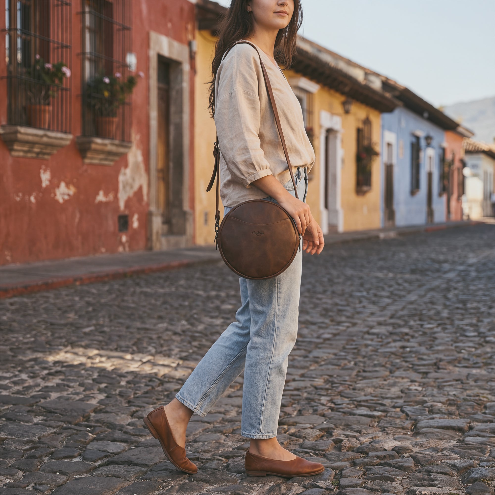 Side perspective of Heather's Female Rounded Crossbody Hand Bag showcasing its elegant silhouette. Made from Full Grain Leather, this zippered handbag for women is both functional and fashionable. Proudly handcrafted in La Antigua Guatemala, the bag demonstrates quality in small batch production, hand cut and hand sewn by skilled artisans.