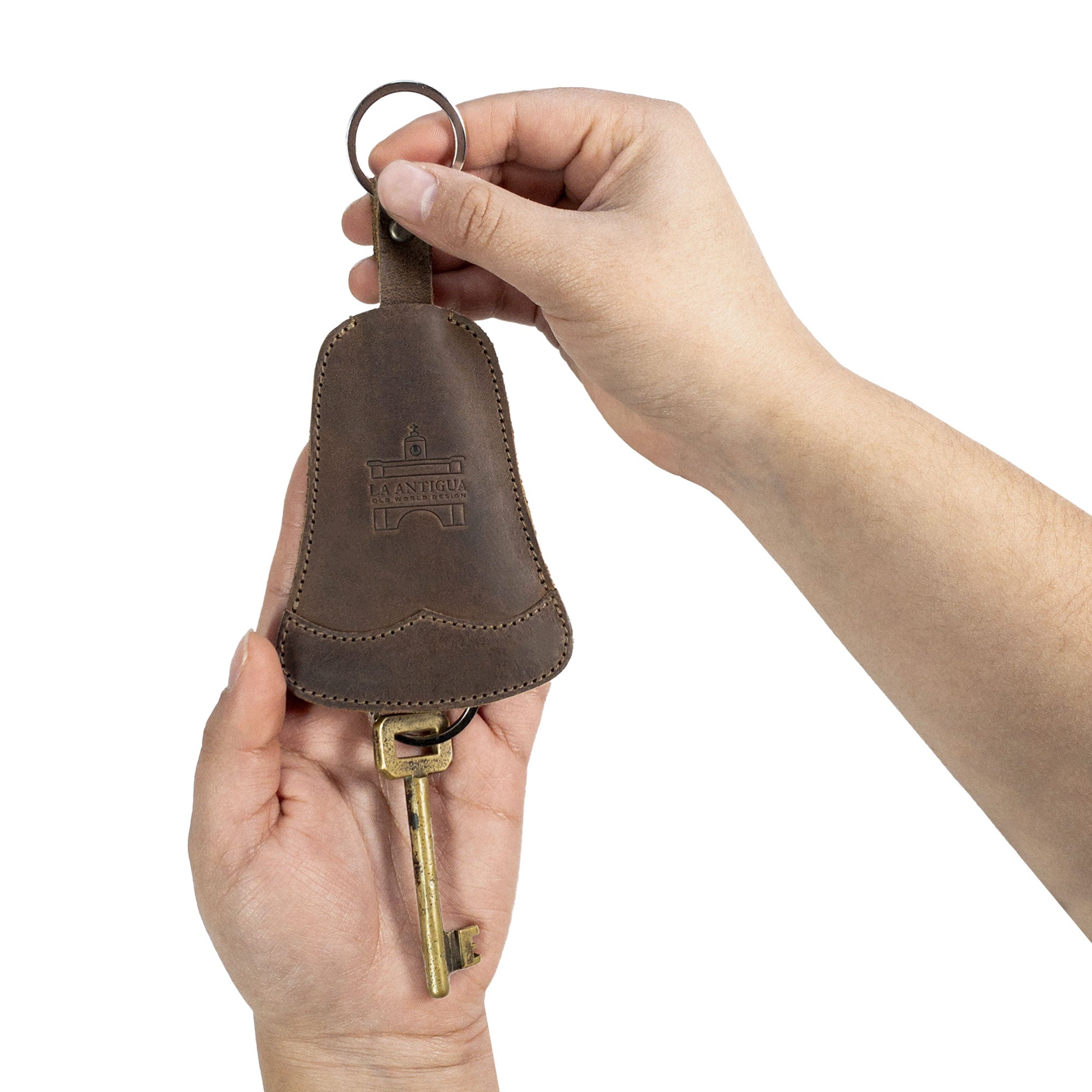 A hand holding the Bell Shape Keychain from La Antigua, demonstrating its practicality as a keyring with strap. This elegant key organizer allows for easy attachment to keys. Crafted from premium full grain leather, this artisan keychain holder emphasizes small batch production and is hand cut, hand sewn, and fire branded, handmade in La Antigua, Guatemala & Oaxaca, Mexico.