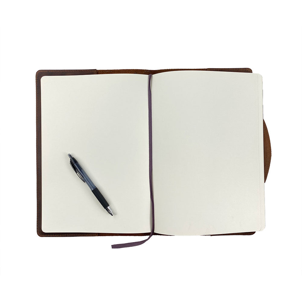 An open view of the Hard Cover Notebook Protector (Notebook NOT Included) by Hide & Drink, showing a blank page and a pen. This journal cover, perfect for Moleskine Hard Cover Sketchbook XXL Size (8.5 x 11 in.), Notebook NOT Included, combines quality craftsmanship with Full Grain Leather, part of StockyardX's small batch production that's hand cut, hand sewn, and fire branded by artisans. Handmade in La Antigua Guatemala & Oaxaca Mexico.