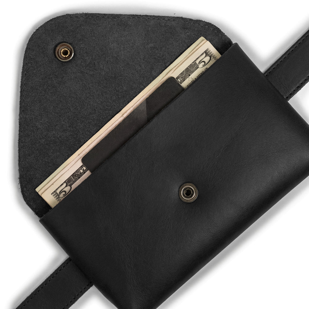 Close-up of the Fancy Fanny Pack by Hide & Drink, filled with cash and earbuds. This full grain leather bag serves as an excellent phone holder and vintage purse, made specially for easy travel for digital nomads. Handcrafted in small batches in La Antigua Guatemala.