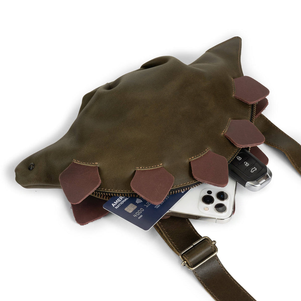Tudi Frudi Leather Dinosaur Stegosaurus Crossbody Jurassic Bag shown holding a phone, wallet and keys, a practical Full Grain Leather Shoulder Bag featuring Small Batch Production, Hand Cut and Hand Sewn Artisan craftsmanship, Fire Branded details by StockyardX, Handmade in La Antigua Guatemala & Oaxaca Mexico.