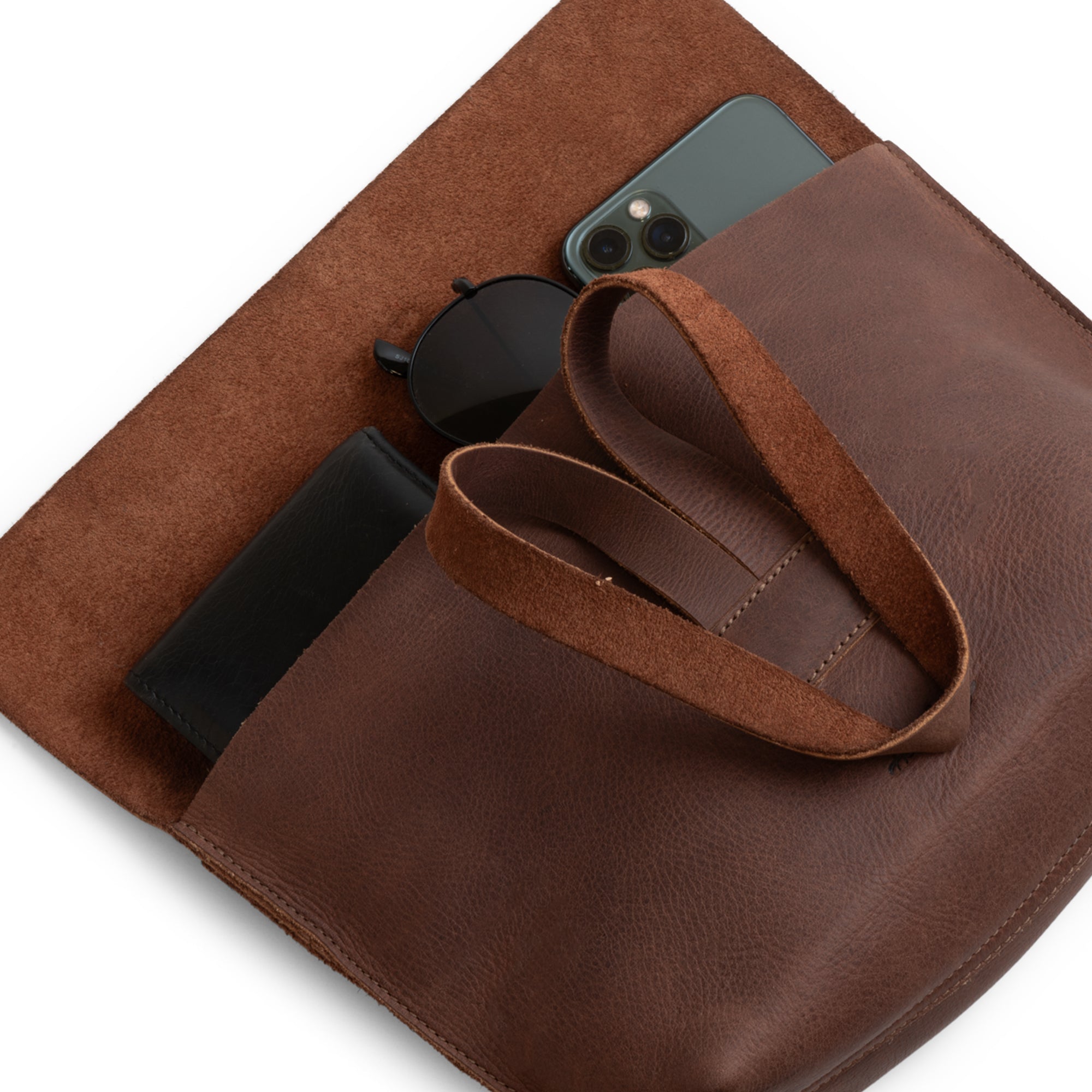 Open Women's Clutch Bag by Heather's, filled with essential items like sunglasses and cosmetics, illustrating its versatility as an accessories pouch. Crafted from Full Grain Leather, this artisan handbag is perfect for travel and everyday convenience.