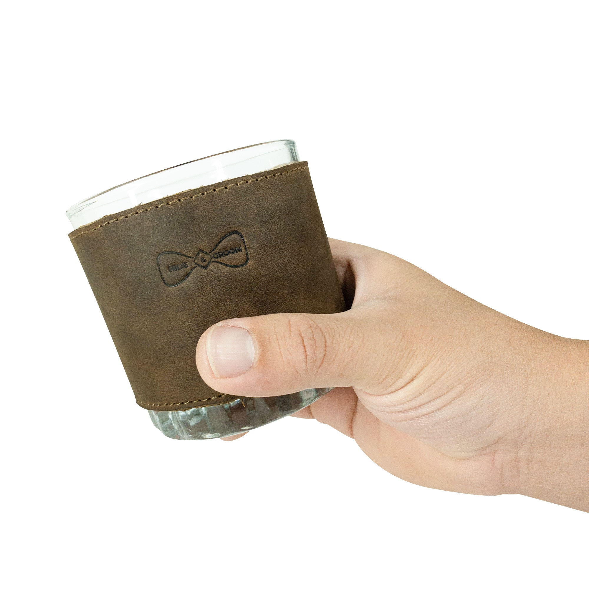 A hand holding one of the Set of 3 Drinking Glass Covers for Groomsmen by Hide & Groom. Perfect for events like weddings, these full grain leather covers are artisanal and suitable for groomsmen, best men, and bachelors. Each cover is made through small batch production methods, hand cut, hand sewn, and fire branded in La Antigua Guatemala & Oaxaca Mexico.