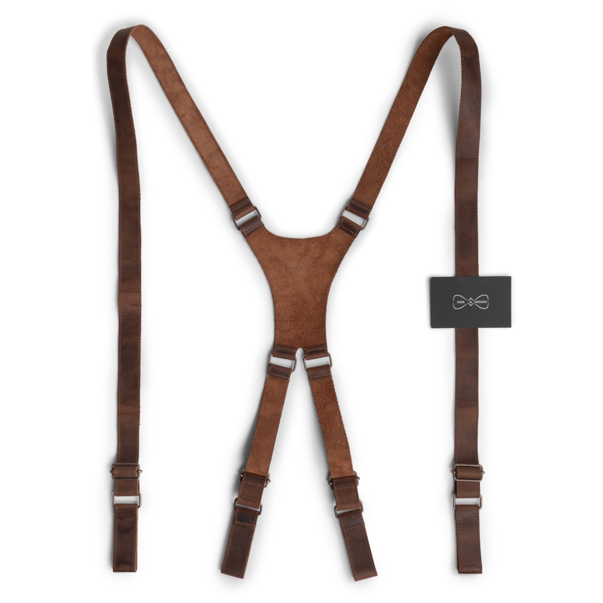 X Back Formal Suspenders by Hide & Groom, showcased with product tags, highlighting their artisanal craftsmanship in full grain leather. These suspenders are perfect for weddings, offering shoulder support and adhering to the groom's dressing code. Handmade in small batches through hand cutting and sewing techniques, they reflect the artisan spirit of La Antigua Guatemala.