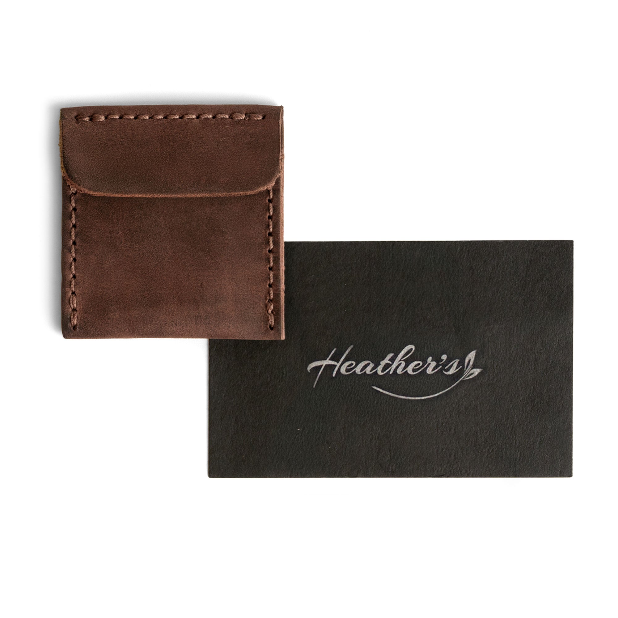 Heather's Wedding Ring Case alongside a branded card, highlighting its elegant design for storing engagement rings. This full grain leather pouch is perfect for bride and groom jewelry storage, ideal for marriage travel or as a ring bearer accessory. Handmade in La Antigua Guatemala & Oaxaca Mexico, each piece is crafted through small batch production, hand cut, and hand sewn to ensure artisanal quality, complete with a fire branded emblem.