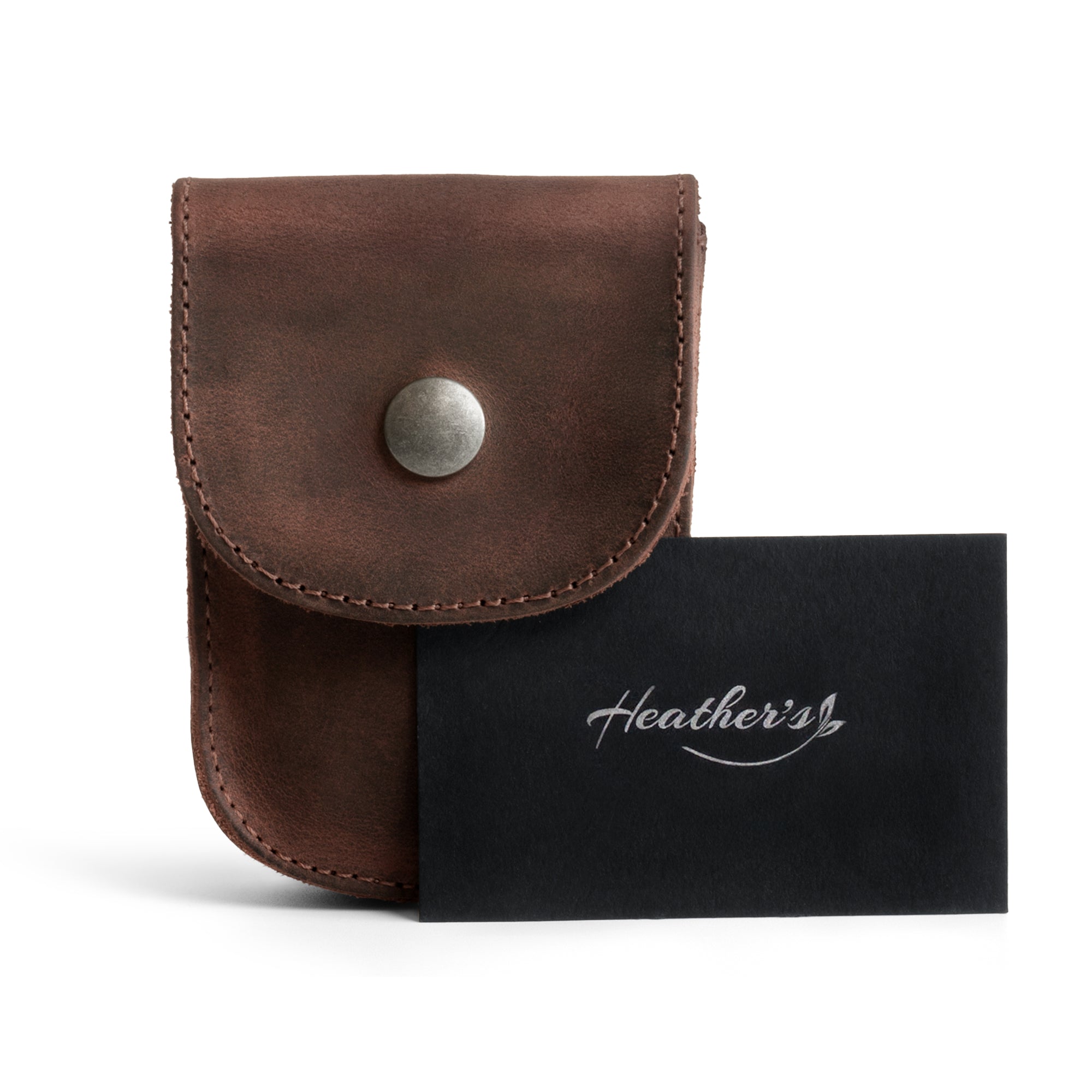 Packaging of the Curvy Waist Bag by Heather's, featuring a card with its origin story. This durable waist bag functions as a holster pouch for coins, change, headphones, and personal items. It conveniently attaches to your belt and is made from luxurious full grain leather. The handmade nature of this product captures small batch production, with each being hand cut, hand sewn, and fire branded by artisans in La Antigua Guatemala & Oaxaca Mexico.
