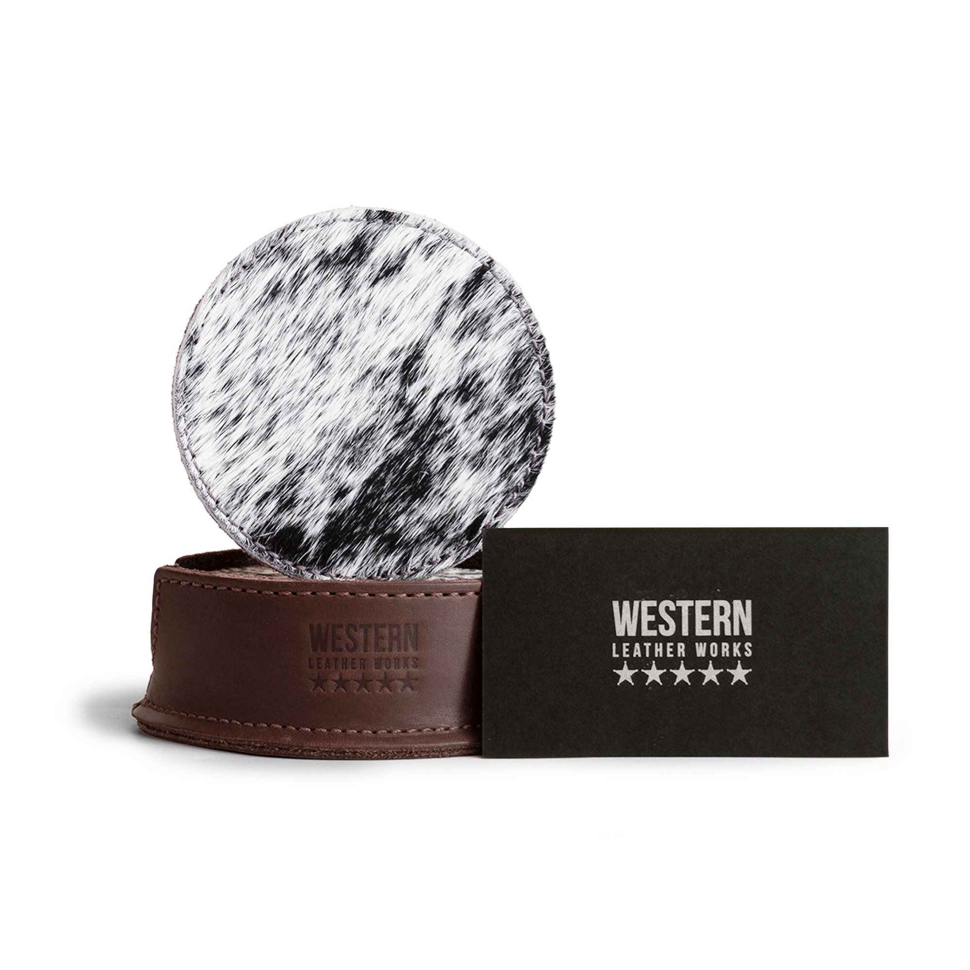 The Western Leather Works logo and a hair-on-hide coaster are presented alongside a card, representing the Set of 6 Circular Coasters for Drinks. This image emphasizes the product's role in providing Glass & Cups Stain Protection while showcasing its Full Grain Leather quality, made through small batch production with hand cut, hand sewn details, and fire branding, highlighting its artisan background from La Antigua Guatemala & Oaxaca Mexico.
