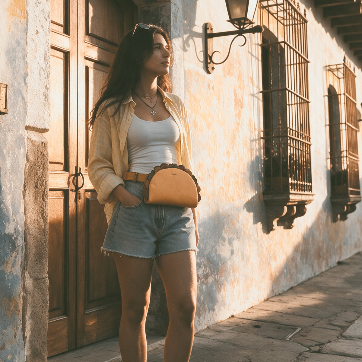 Model wearing the Hide & Drink Taco Fanny Pack as a waist bag with a casual outdoor outfit on a sunlit street. The tan full grain leather Taco Fanny Pack is a fun belt bags accessory, zippered bags travel carrier, outdoor waist pouch, carry on case, and travel accessory from StockyardX, made with small batch production, hand cut, hand sewn, fire branded artisan craftsmanship, handmade in La Antigua Guatemala & Oaxaca Mexico.