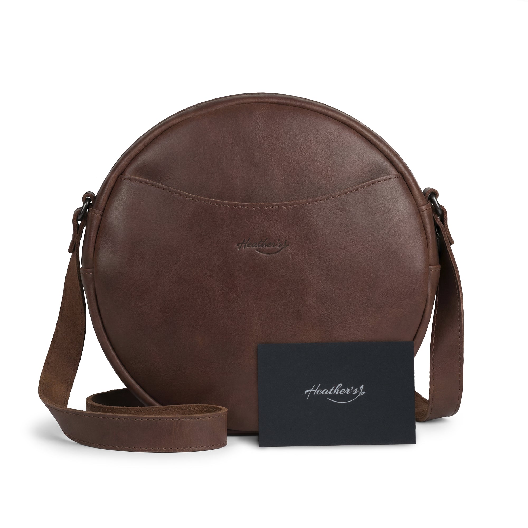 Heather's Female Rounded Crossbody Hand Bag with a note peeking out, depicting its practical use. Crafted from Full Grain Leather, this zippered handbag for women and shoulder bag for girls is both stylish and functional. Handmade in La Antigua Guatemala, showcasing the artisan's hand cut, hand sewn, and small batch production techniques.