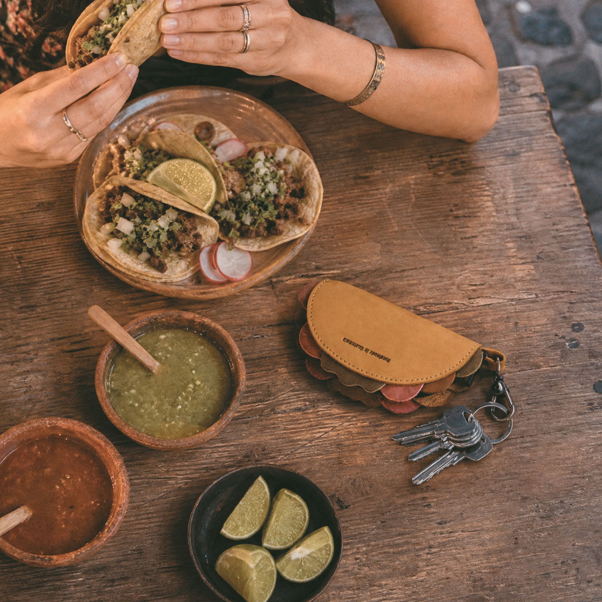 Hide & Drink Taco Zip Pouch Bag Charm Key Chain worn on a brown leather crossbody bag while traveling, showing its playful taco shape and practical everyday style. Taco Zip Pouch Bag Charm Key Chain Full Grain Leather, StockyardX, Small Batch Production, Hand Cut, Hand Sewn, Fire Branded, Artisan, Handmade in La Antigua Guatemala & Oaxaca Mexico.