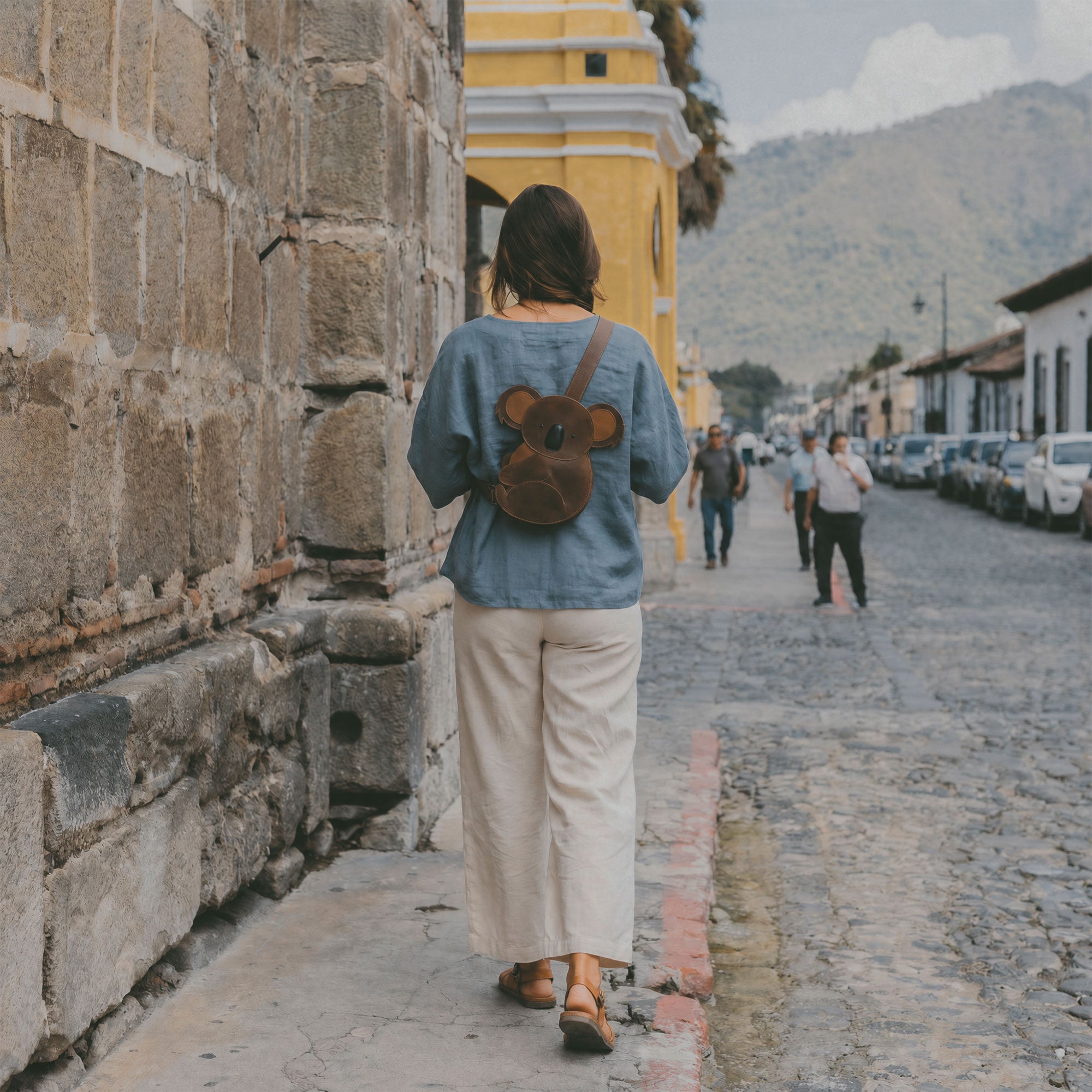 Woman walking away wearing the Tudi Frudi Leather Koala Crossbody Bag, demonstrating its practicality as a chic shoulder bag. This handmade bag, crafted from full grain leather, is suitable for both men and women and features small batch artisan techniques from La Antigua Guatemala and Oaxaca Mexico.