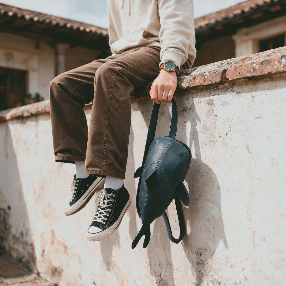 Person carrying the Hide & Drink Leather Shark Backpack (Megalodon) by its top handle while traveling outdoors, highlighting its unique shark silhouette. Leather Shark Backpack (Megalodon), Casual Bag, Messenger Bag, Travel Bag for Men and Women, Full Grain Leather, StockyardX, Small Batch Production, Hand Cut, Hand Sewn, Fire Branded, Artisan, Handmade in La Antigua Guatemala & Oaxaca Mexico.