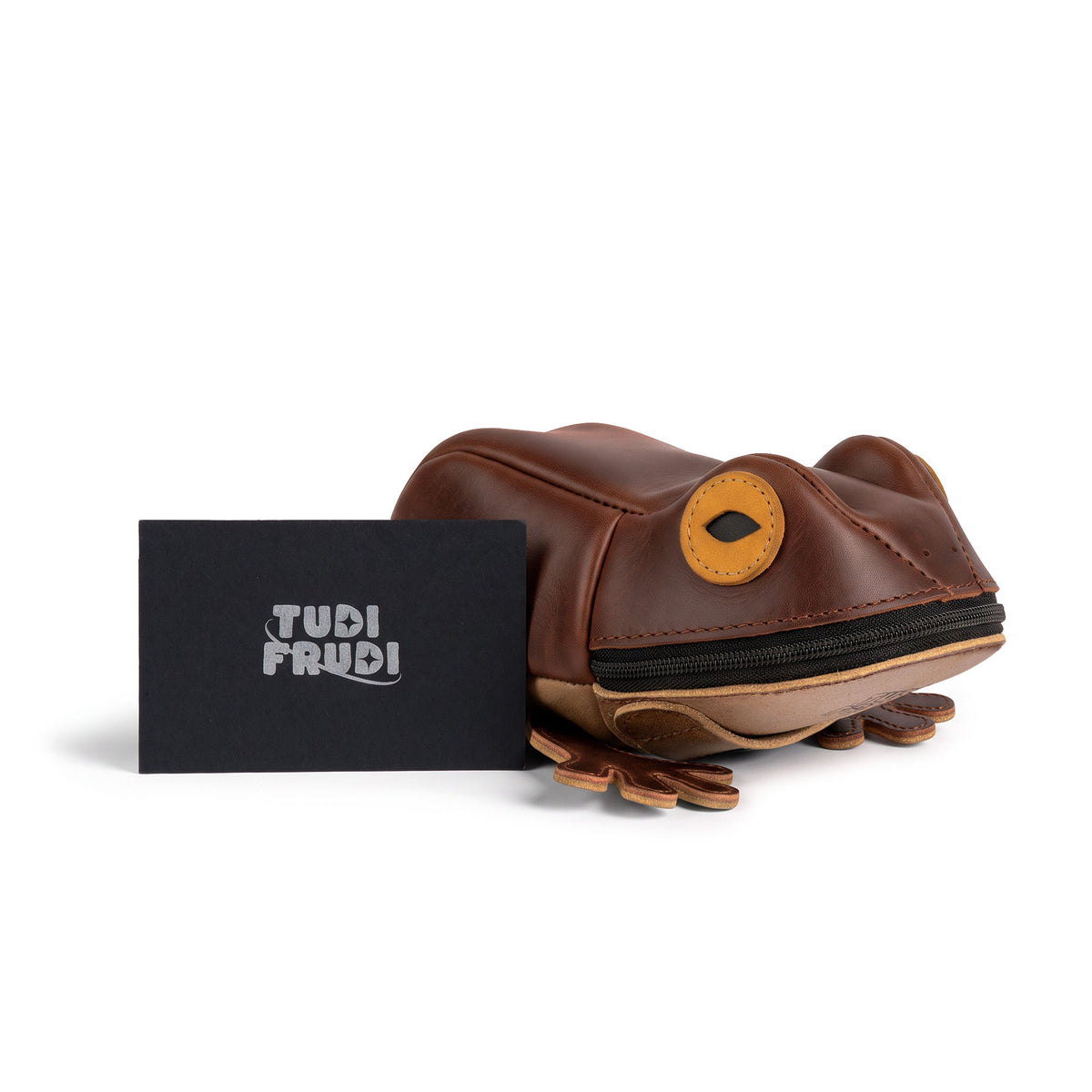 Tudi Frudi Frog Pouch displayed beside branded packaging, highlighting its brown leather frog shape and zippered design as a Frog-Shaped Pouch, Cable Organizer, and Small Accessory Case; Zippered Cash Holder Wallet for Coins and Change Purse, made for Pouches for Men and Women. Full Grain Leather product from StockyardX, created through Small Batch Production, Hand Cut and Hand Sewn craftsmanship, Fire Branded, Artisan, Handmade in La Antigua Guatemala & Oaxaca Mexico.