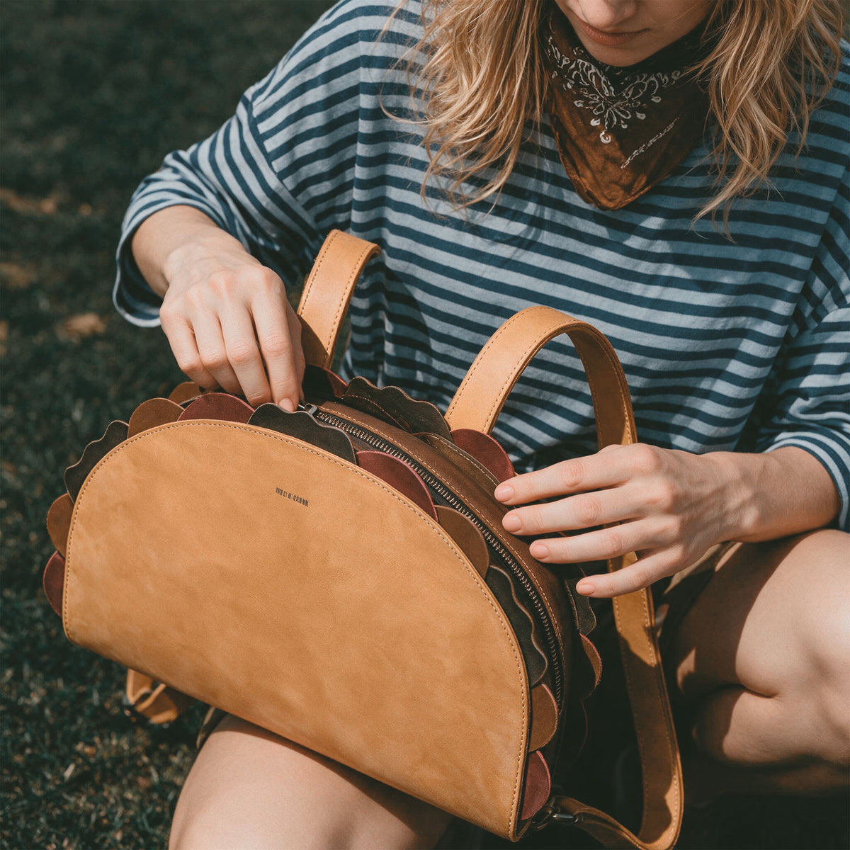 Woman opening the Hide & Drink Taco Backpack outdoors, a Taco Backpack and Fashion Zippered Bag with Carry Pack with Adjustable Shoulder Straps, Fun Carryalls style, Casual Daypack design, and Travel Accessory appeal; made from Full Grain Leather by StockyardX through Small Batch Production, Hand Cut and Hand Sewn with Fire Branded Artisan details, Handmade in La Antigua Guatemala & Oaxaca Mexico.