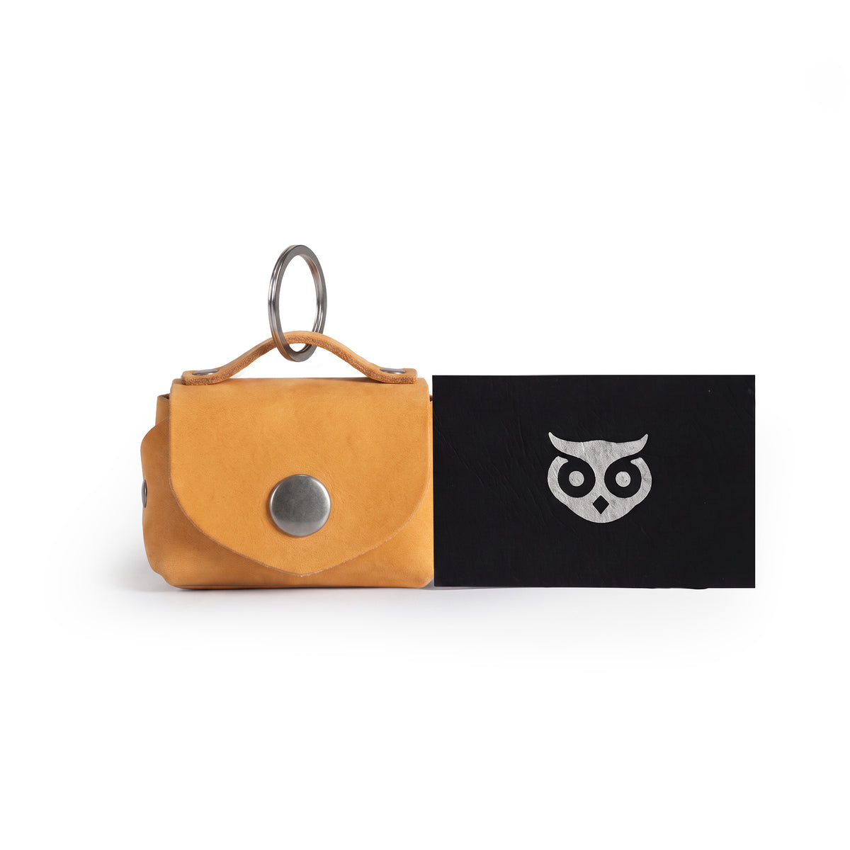 Top view of the mustard Tiny Handbag Keychain by Hide & Drink alongside its unique packaging, showcasing the Tiny Handbag with Key Ring Holder crafted from Full Grain Leather. This artisan product emphasizes Small Batch Production, and is Hand Cut, Hand Sewn, and Fire Branded, highlighting its Handmade craftsmanship from La Antigua Guatemala & Oaxaca Mexico.