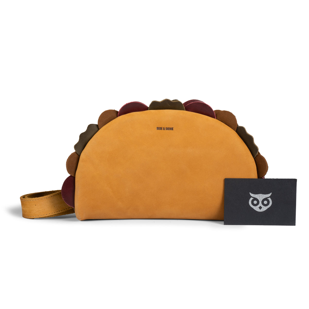 Front product view of the Hide & Drink Taco Fanny Pack in tan full grain leather displayed with its branded packaging card and adjustable waist strap. This playful waist bag is part of the fun belt bags and zippered bags collection, serving as a travel carrier, outdoor waist pouch, carry on case, and travel accessory. The StockyardX Taco Fanny Pack features small batch production, hand cut, hand sewn, fire branded artisan craftsmanship, handmade in La Antigua Guatemala & Oaxaca Mexico.
