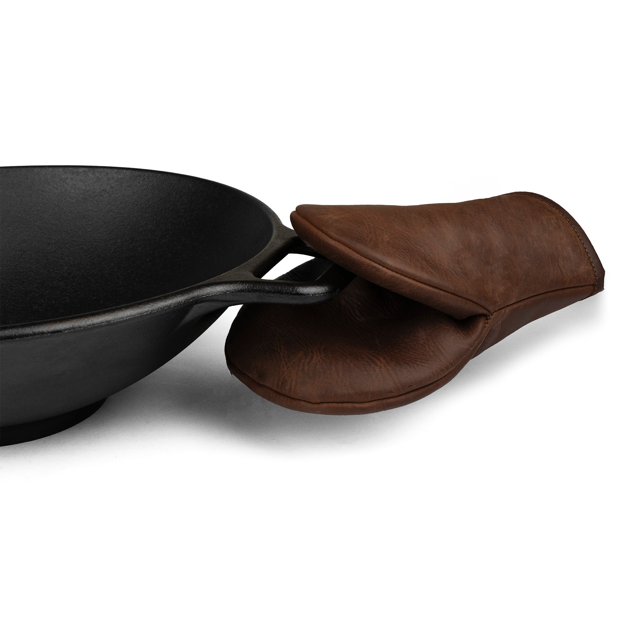 Cast Leather Co. Dual-Hand Leather Oven Mitt resting on a black cast iron pan, showcasing the perfect Oven Glove Heat Resistant that protects hands while baking and cooking. This kitchen accessory features Full Grain Leather, well-crafted through small batch production, hand cut, and sewn. Artisan quality handmade in La Antigua Guatemala & Oaxaca Mexico.