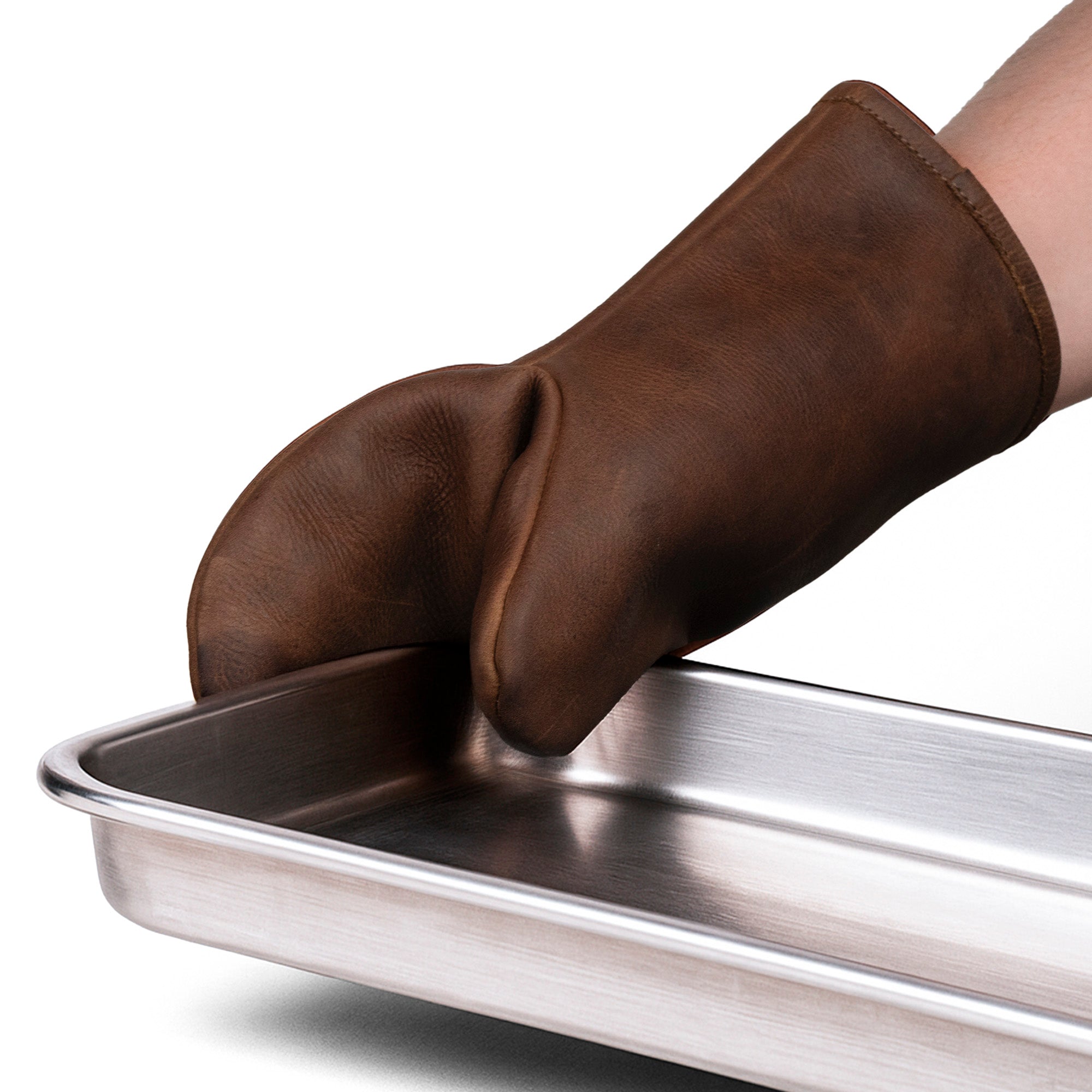 A hand wearing the Cast Leather Co. Oven Mitt Heat Resistant gripping a metal tray. This Single Oven Mitt Glove Heat Resistant is a perfect potholder for the kitchen, made from full grain leather. StockyardX offers this kitchen cooking accessory crafted through small batch production, using hand cut and hand sewn techniques, ensuring quality and durability. Artisan and handmade in La Antigua Guatemala & Oaxaca Mexico.